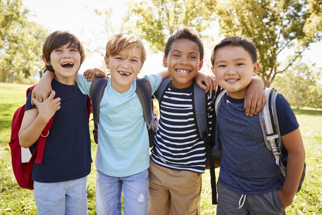A diverse group of young schoolboys smiling together outdoors with backpacks, highlighting the foundation of health curiosity from early childhood.
