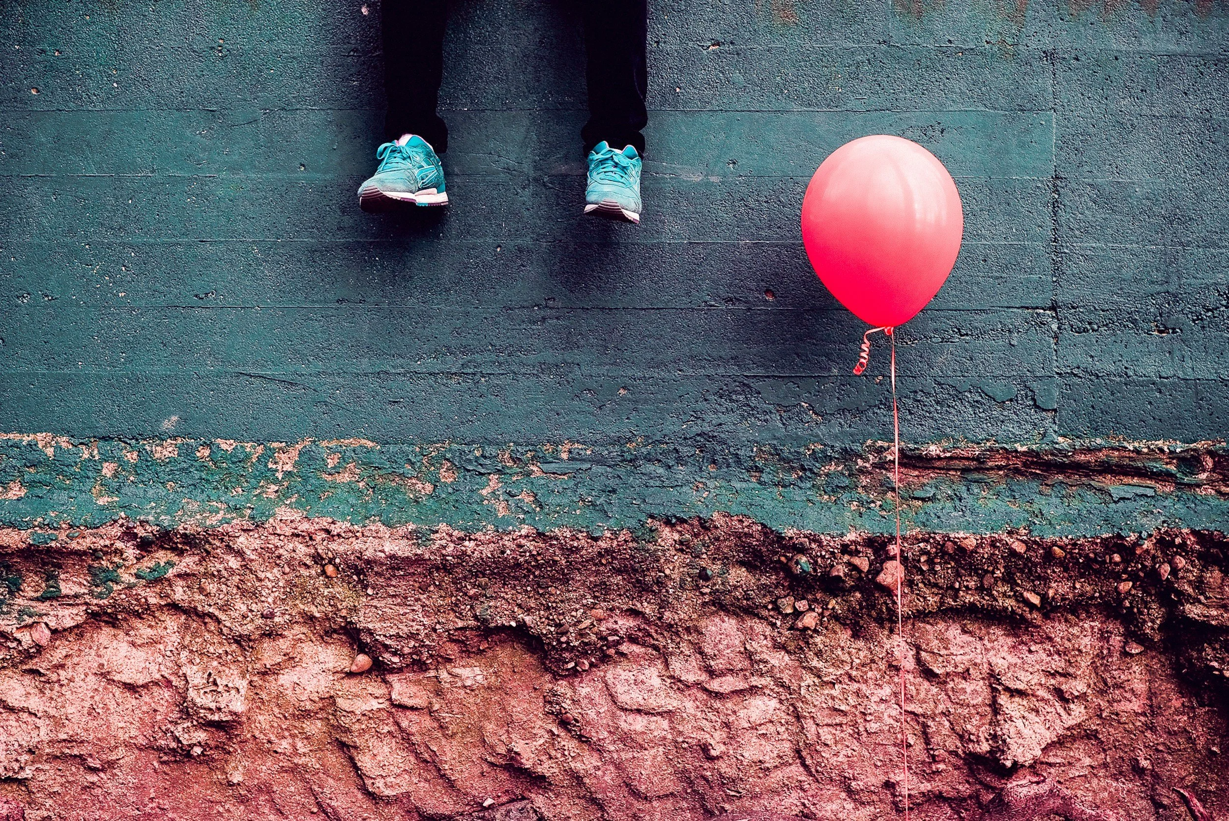 An abstract conceptual art piece showing dangling feet next to a pink balloon, visualizing physical suspension and pressure systems.