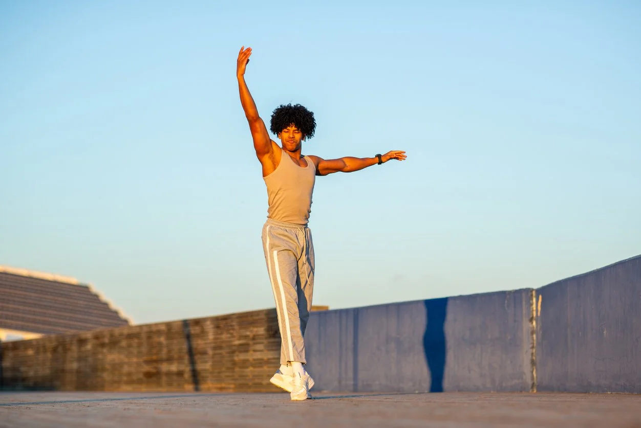 An African American male ballet dancer mid-leap in a bright studio, celebrating physical freedom, vitality, and full-body health curiosity