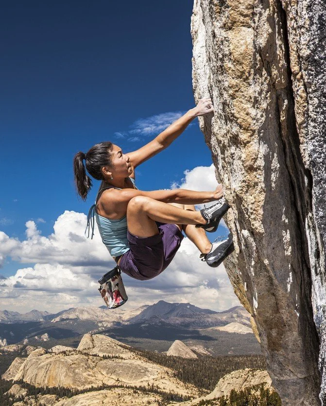 A woman rock climbing an outdoor cliff face, symbolizing high-performance tracking and health curiosity biometrics.