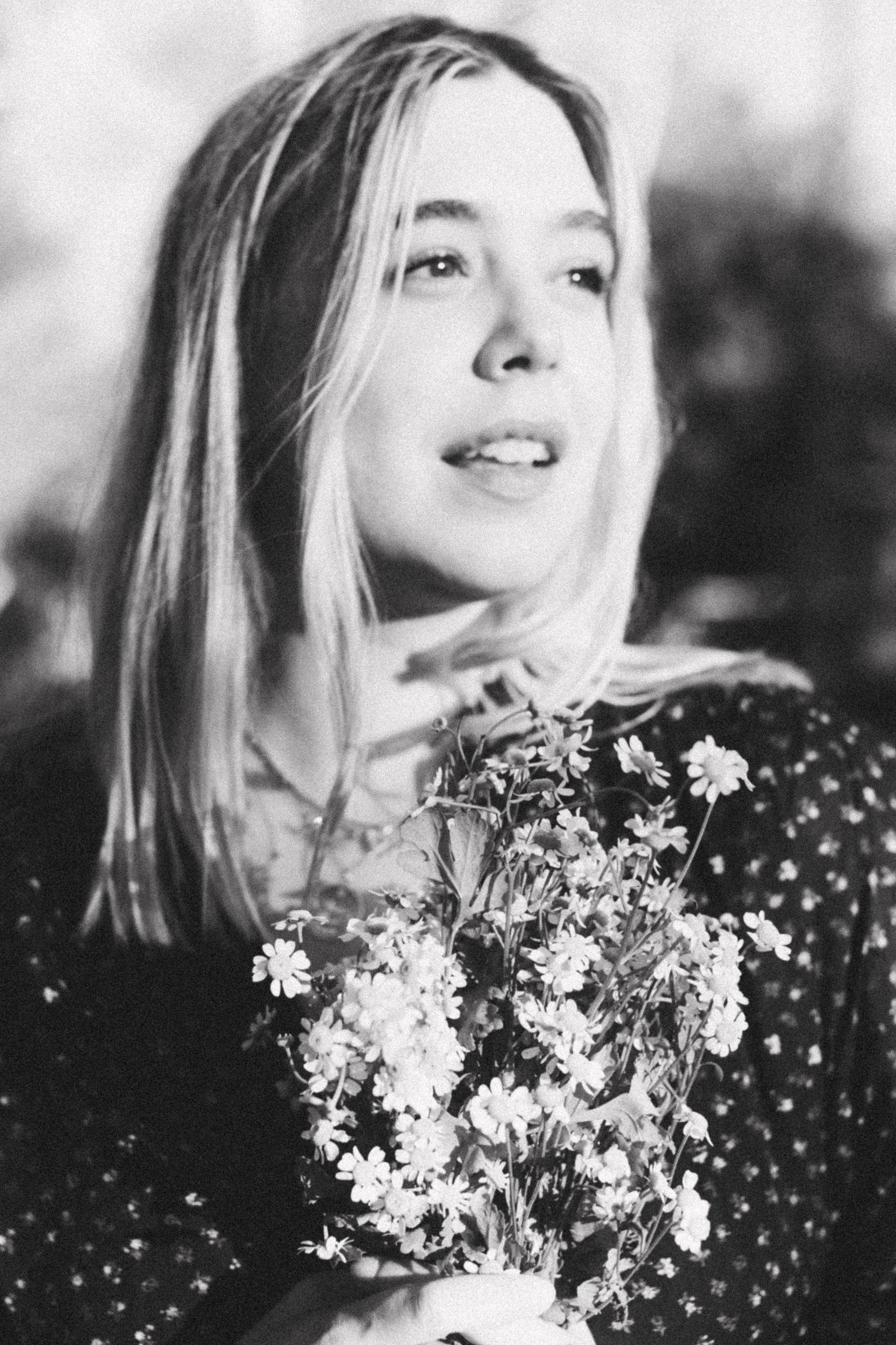 Black-and-white creative portrait of a woman holding a bouquet of small flowers.
