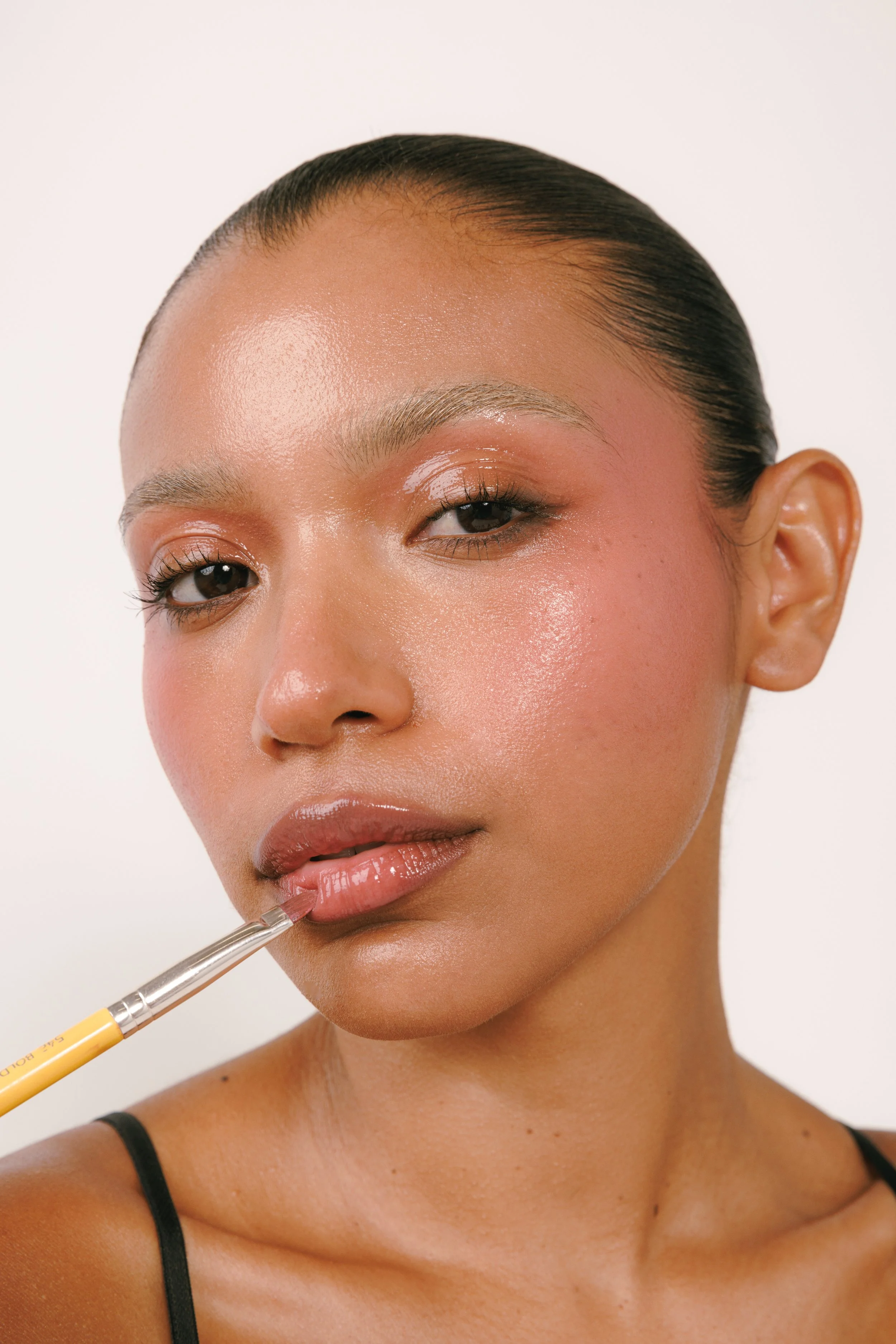 Beauty editorial series featuring a model with luminous, glittering makeup and glossy lips, photographed against a clean white background with makeup brushes.