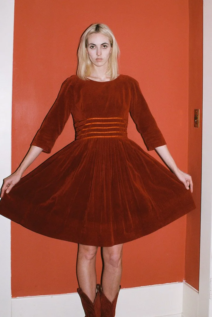 Fashion model wearing a vintage red velvet dress with a full skirt, standing against a red wall.