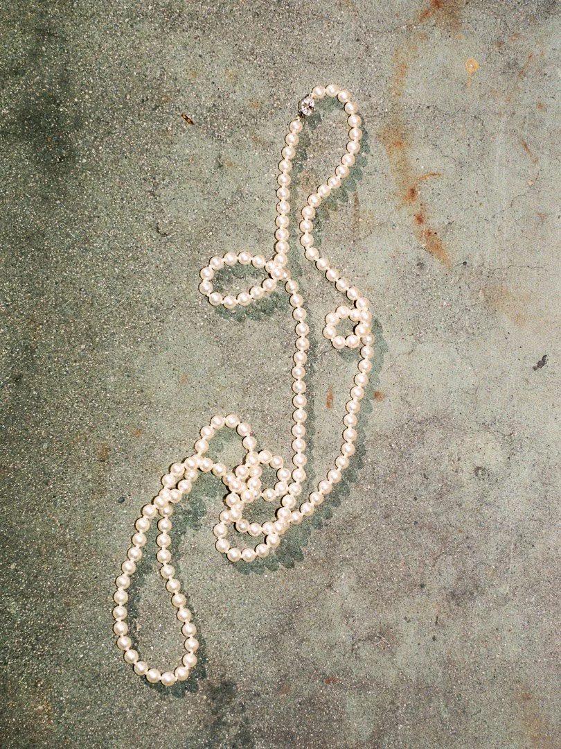 String of white pearl beads arranged in the shape of a treble clef on a gray concrete surface.