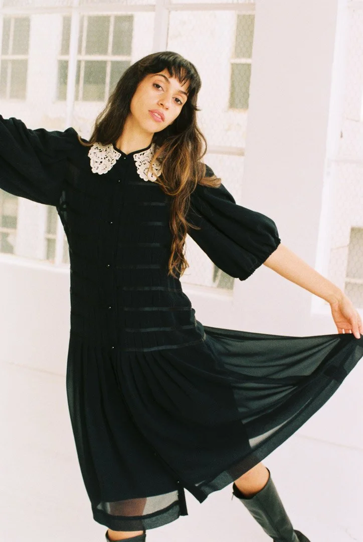 Editorial-style portrait of a fashion model wearing a vintage dress beside studio windows.