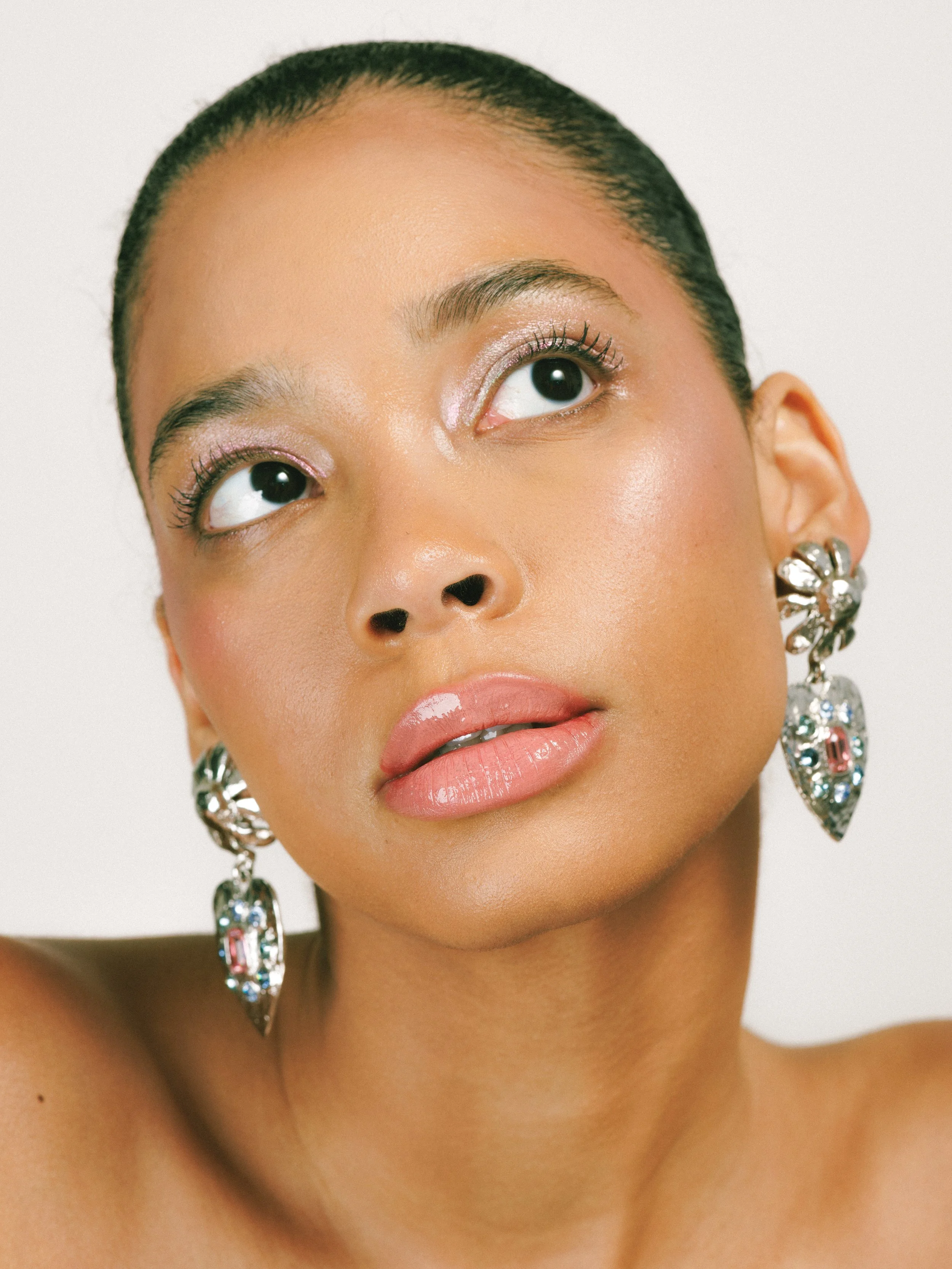 Close-up portrait of a fashion model wearing statement earrings and makeup, with her head tilted slightly upward.
