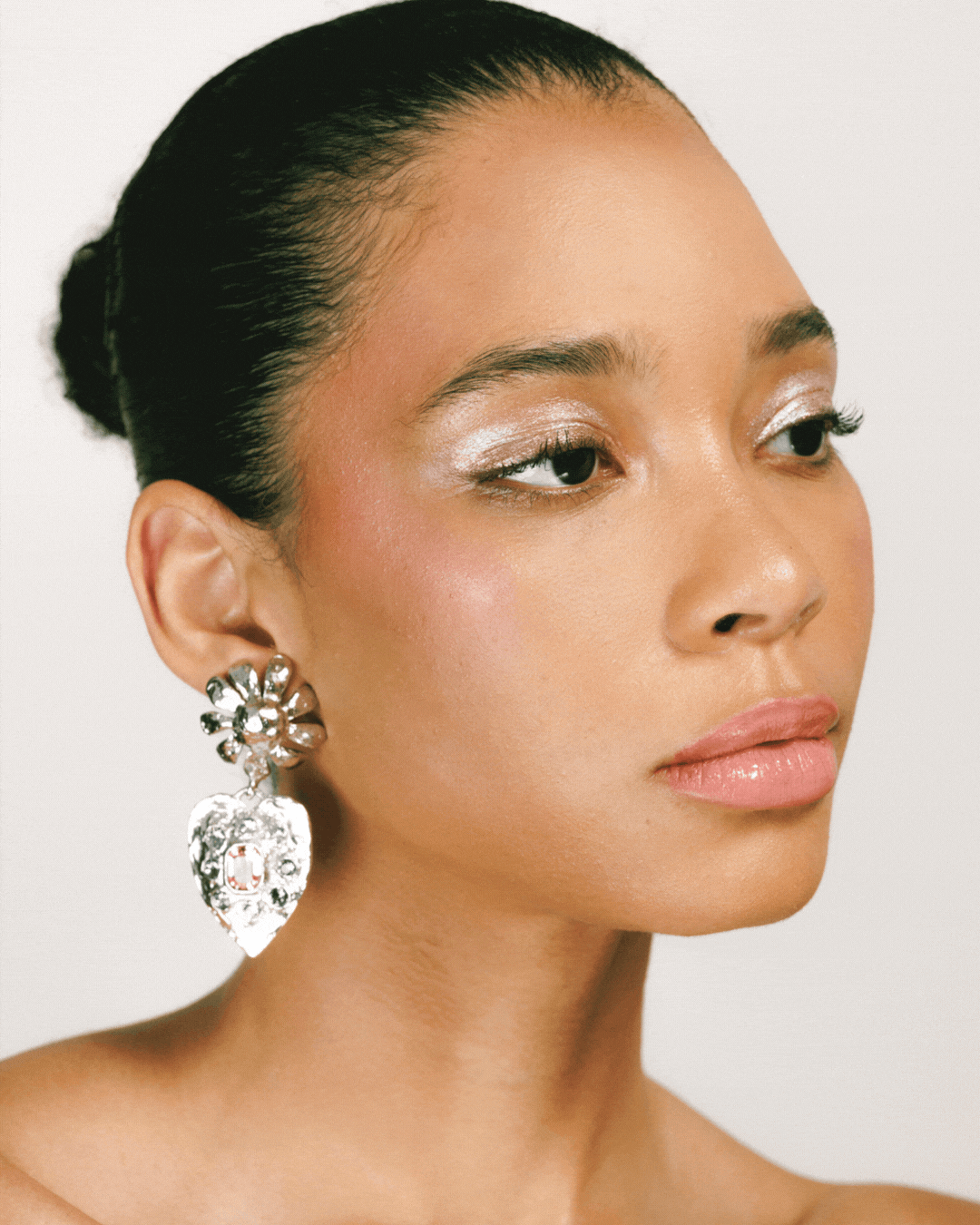 Close-up portrait of a fashion model wearing silver earrings and shimmery eye makeup against a plain background.