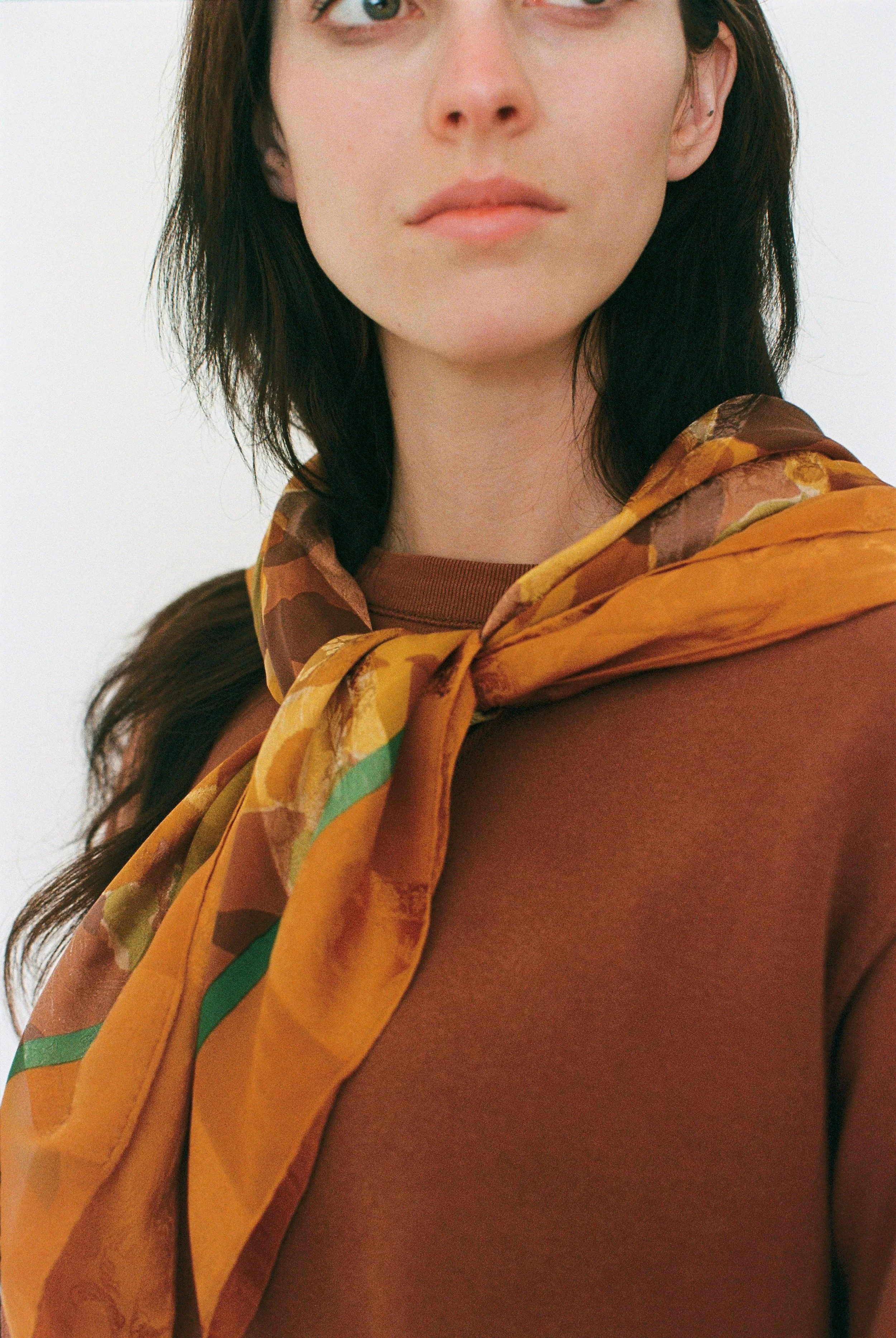 Close-up of a fashion model with dark hair and bare shoulders wearing a patterned yellow and brown scarf.