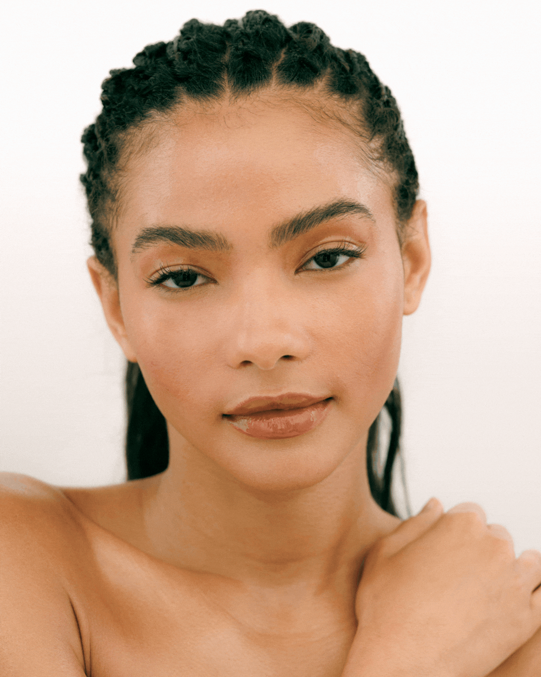 Close-up portrait of a fashion model with braided hair and natural makeup, touching her shoulder with unique expressions.