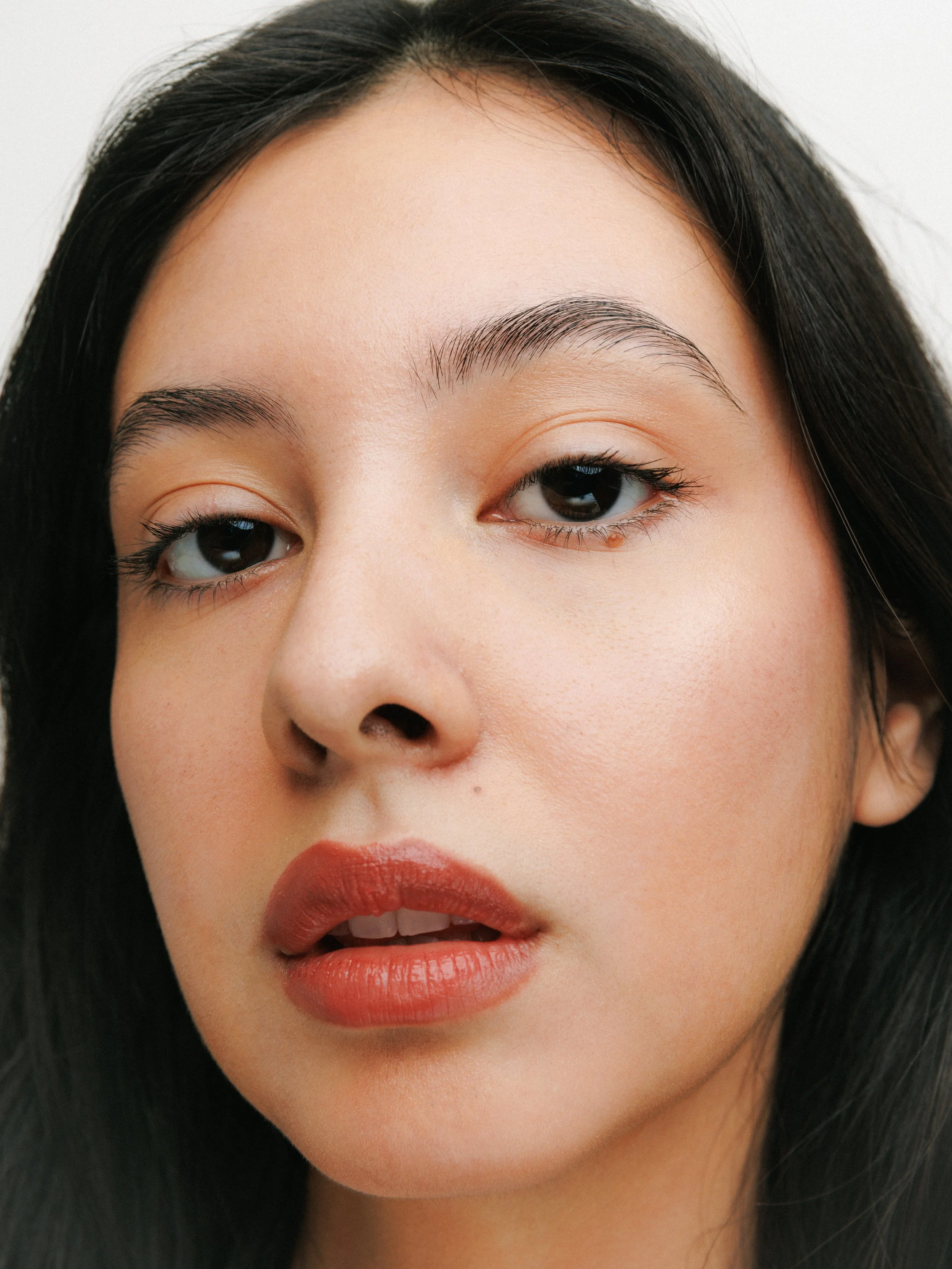 Close-up portrait of a fashion model with dark hair wearing makeup and red lipstick.
