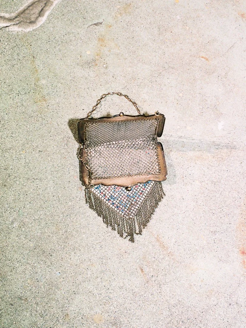 Small metallic embellished purse with a chain strap resting on a rough, sandy surface.