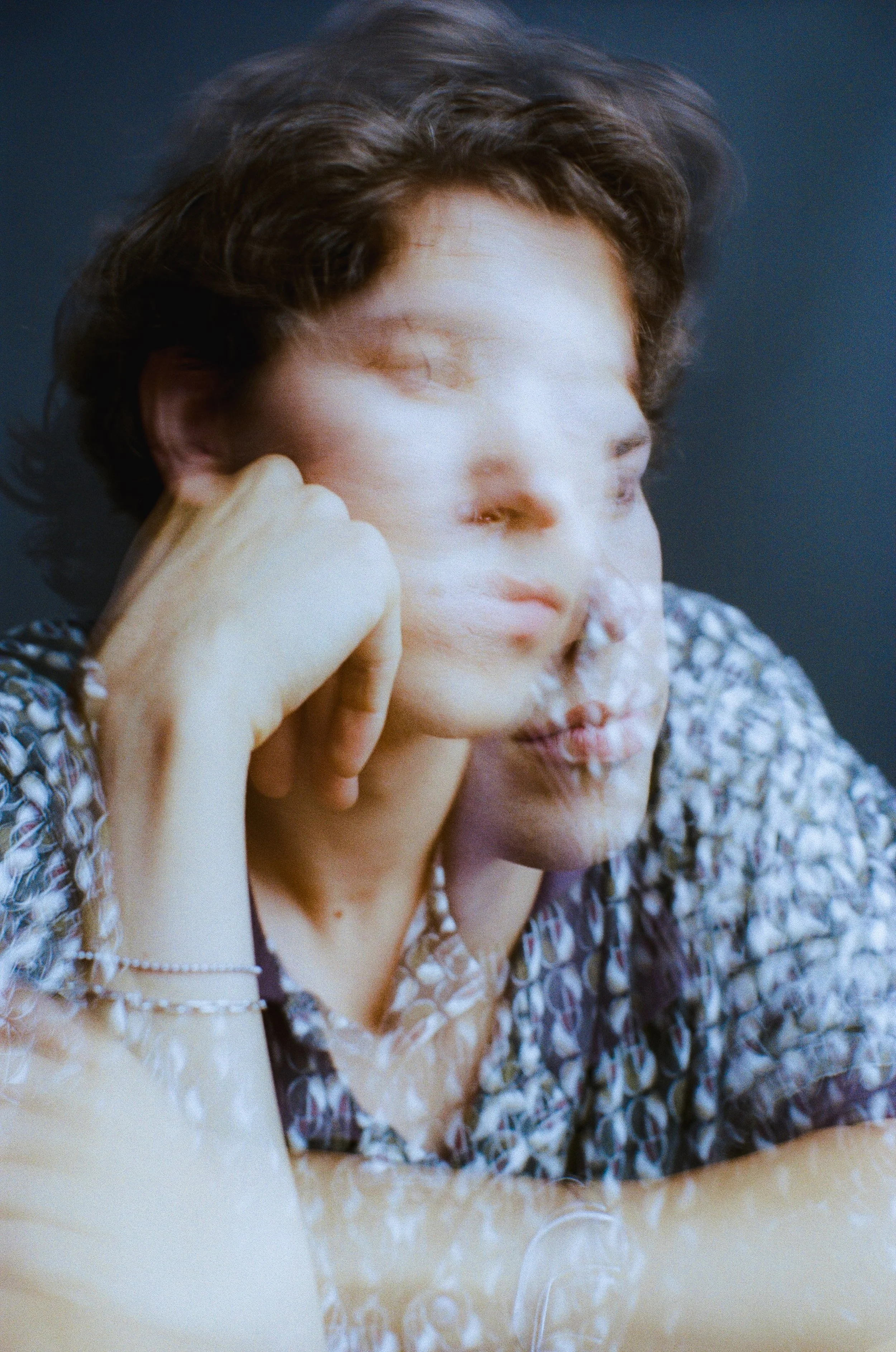Portrait of a man resting his head on his hand, photographed with a soft double-exposure effect against a dark blue background, captured on film.