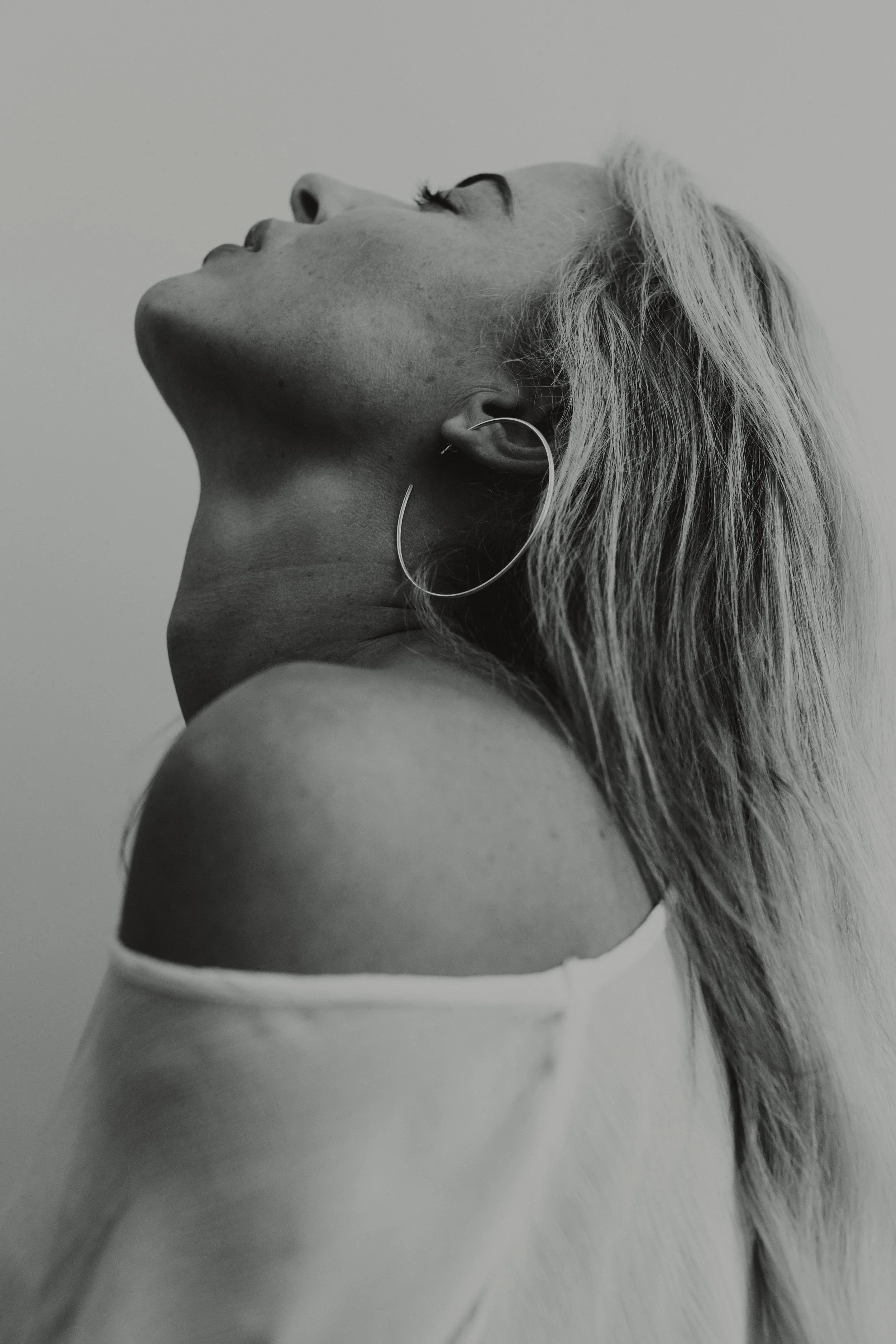 Black and white photo of a woman with long hair, wearing a large hoop earring, with her head tilted back and eyes closed.