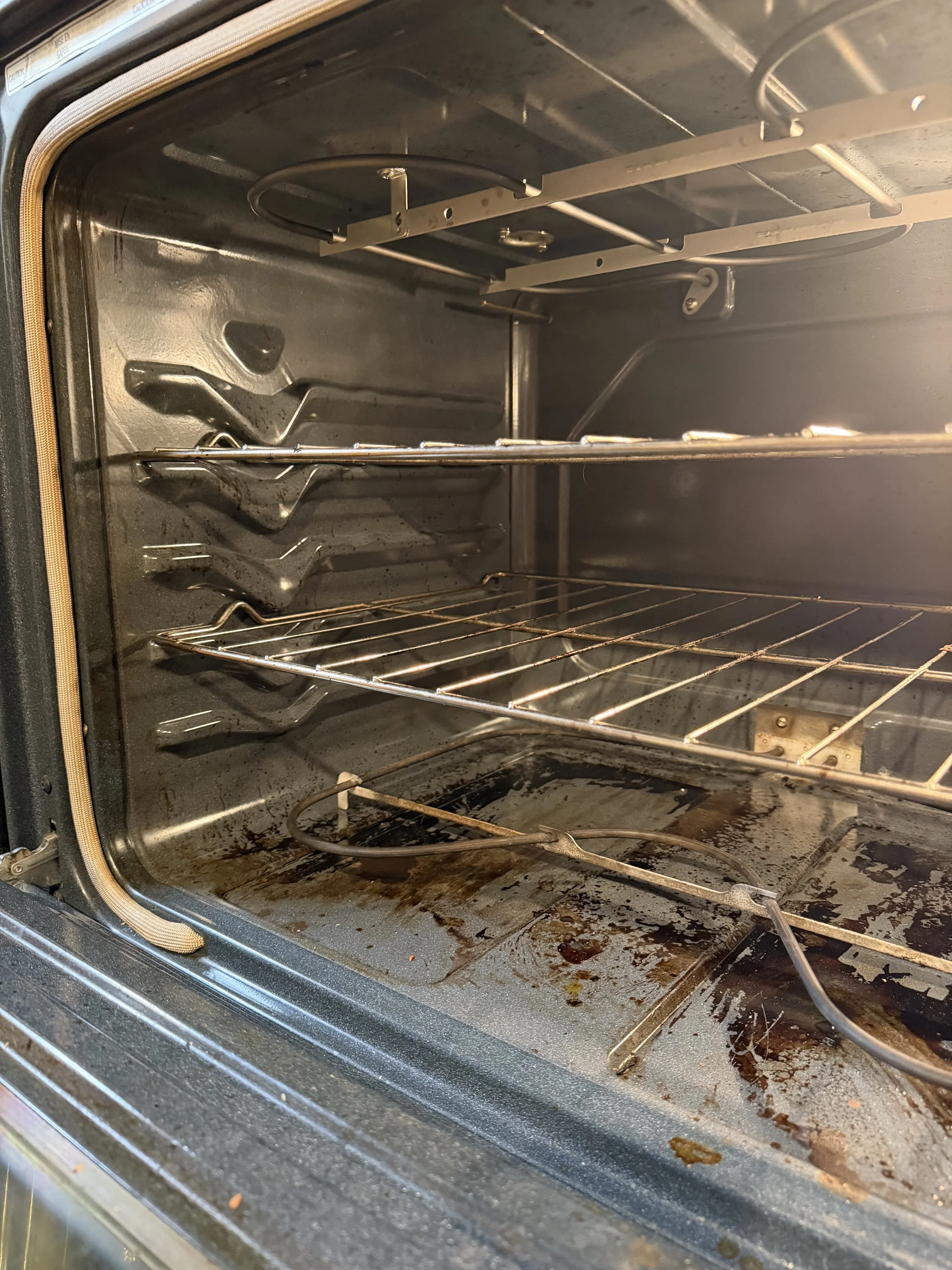 Dirty oven with food residue, grime, and burnt spots on the interior surfaces, racks, and bottom.
