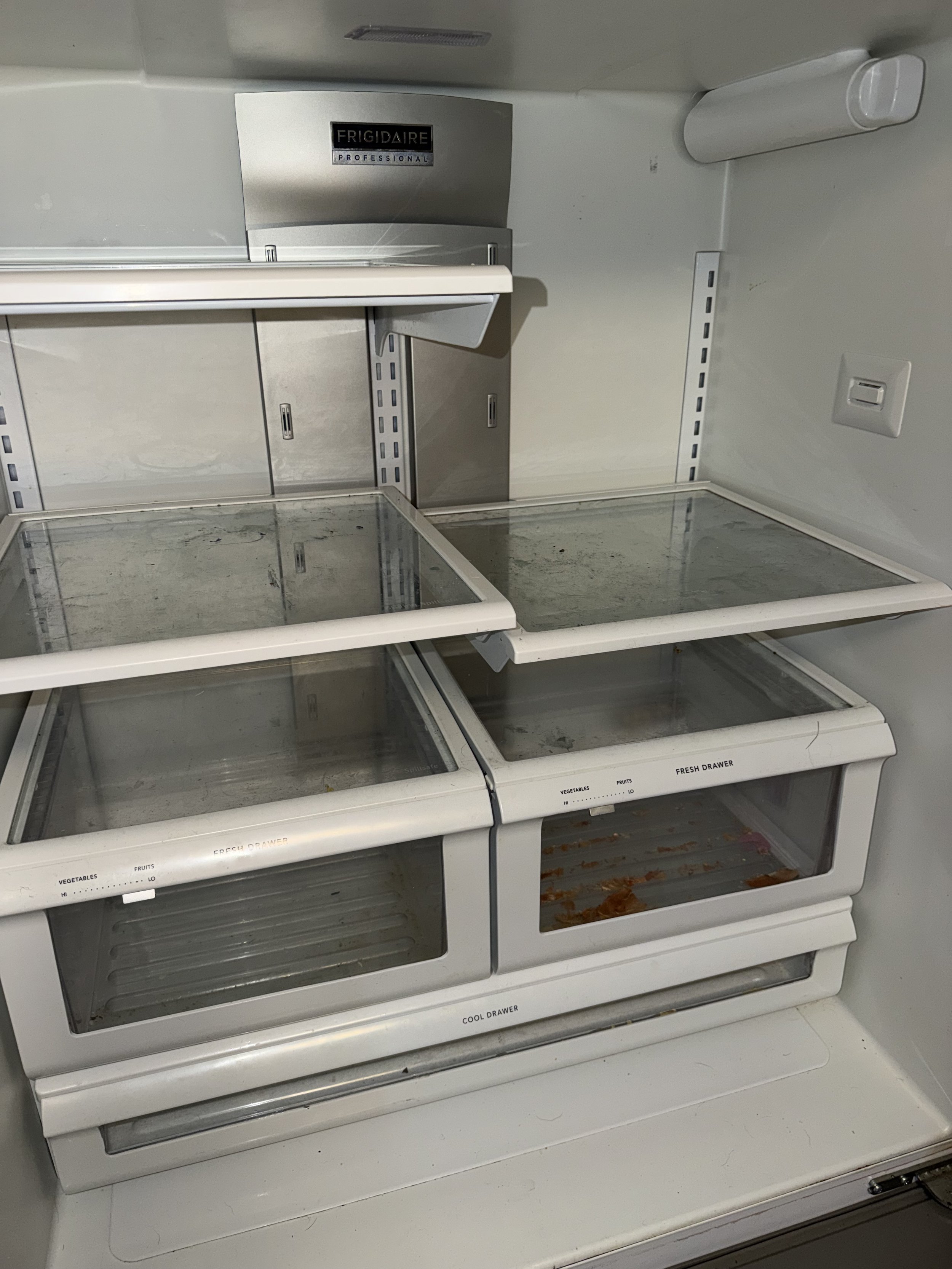 Empty refrigerator with dirty glass shelves, some stains, and empty drawers.