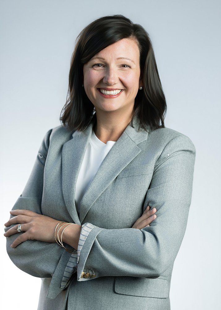 A woman with shoulder-length dark hair smiling, wearing a light gray blazer and a white top, with her arms crossed.