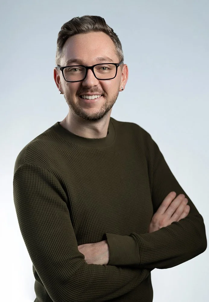 Portrait of a smiling man with glasses, crossed arms, wearing a dark green sweater, in a professional photo studio.