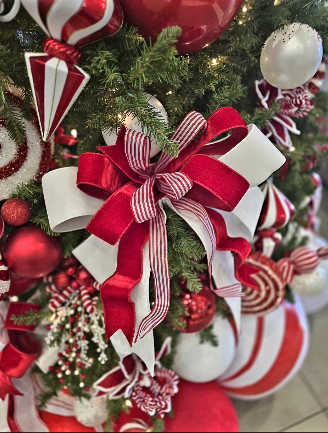 Close-up of a Christmas tree decorated with red and white ribbons, bows, and ornaments.
