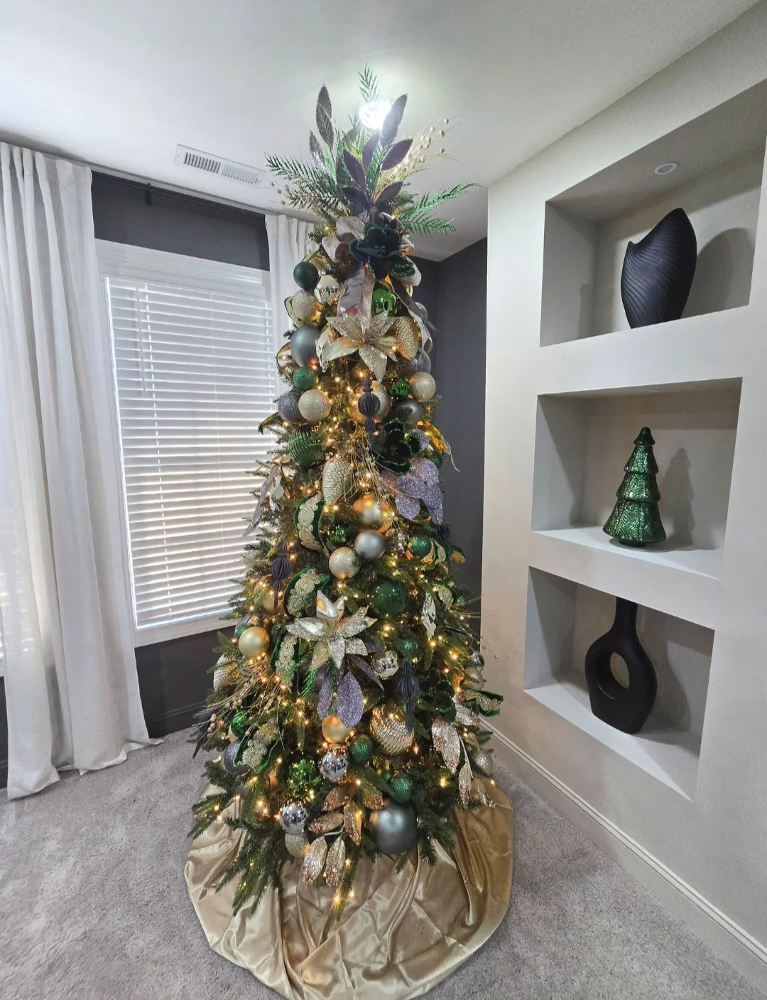 Decorated Christmas tree with gold and green ornaments, ribbons, and lights in a living room corner.