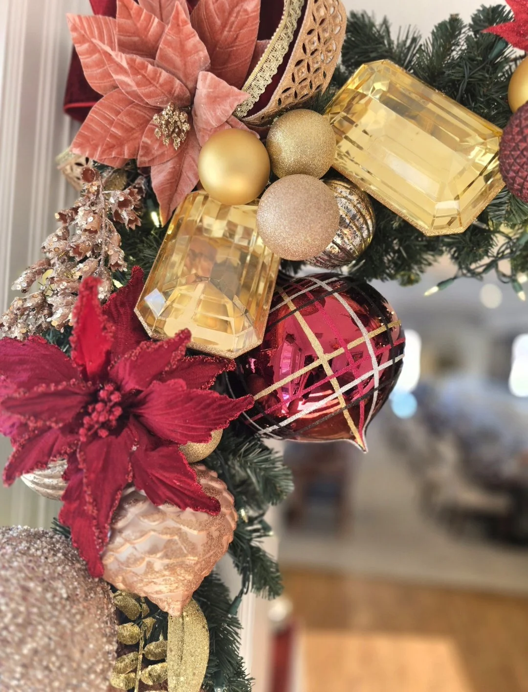 Close-up of a decorated Christmas garland featuring gold, pink, and red ornaments, including poinsettias, glittery baubles, and sparking accents.