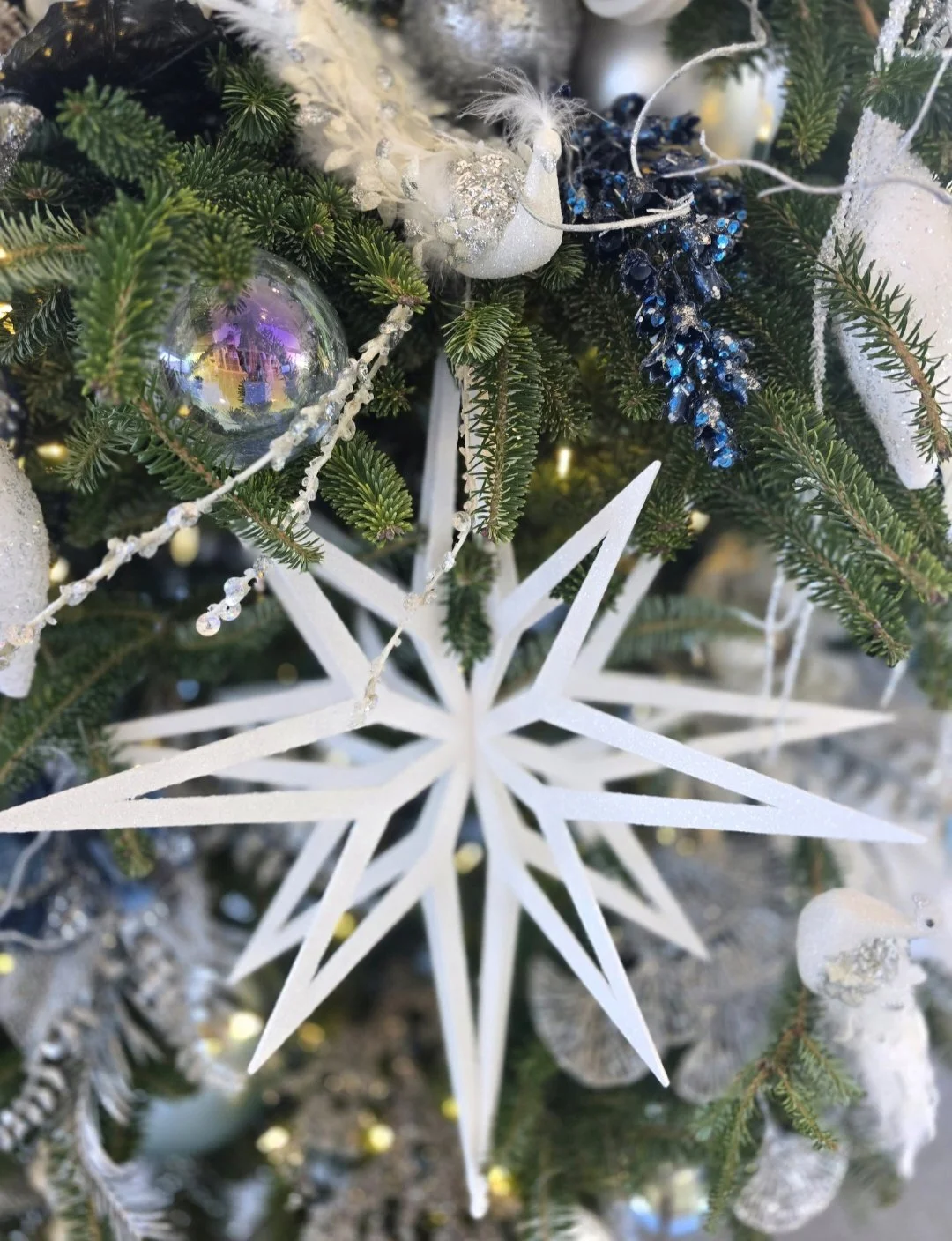 Close-up of a decorated Christmas tree with ornaments, including a large white snowflake, a silver ball, and various white and blue decorations.