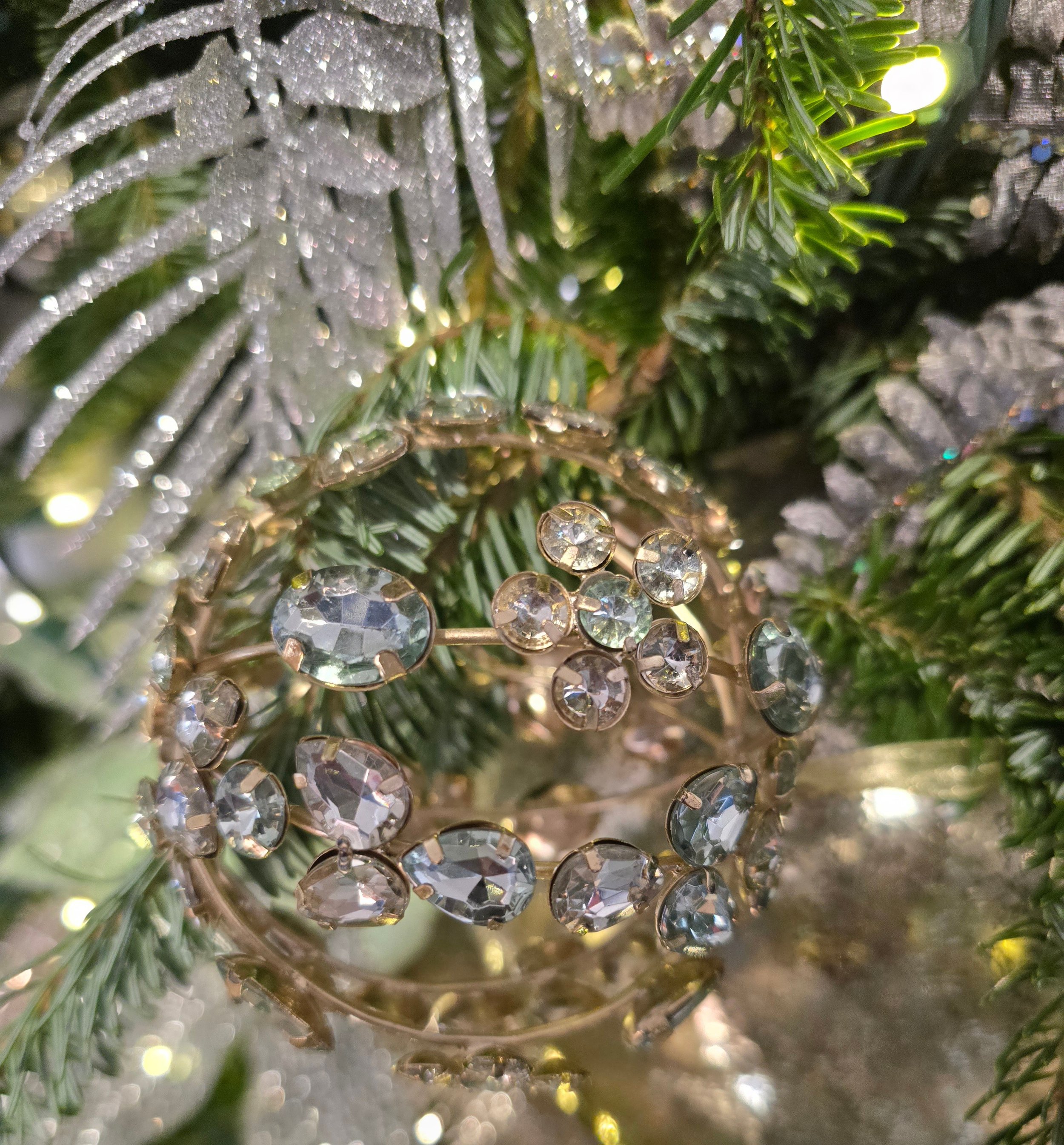 Close-up of a decorated Christmas tree with green branches, fairy lights, and hanging crystal ornaments.