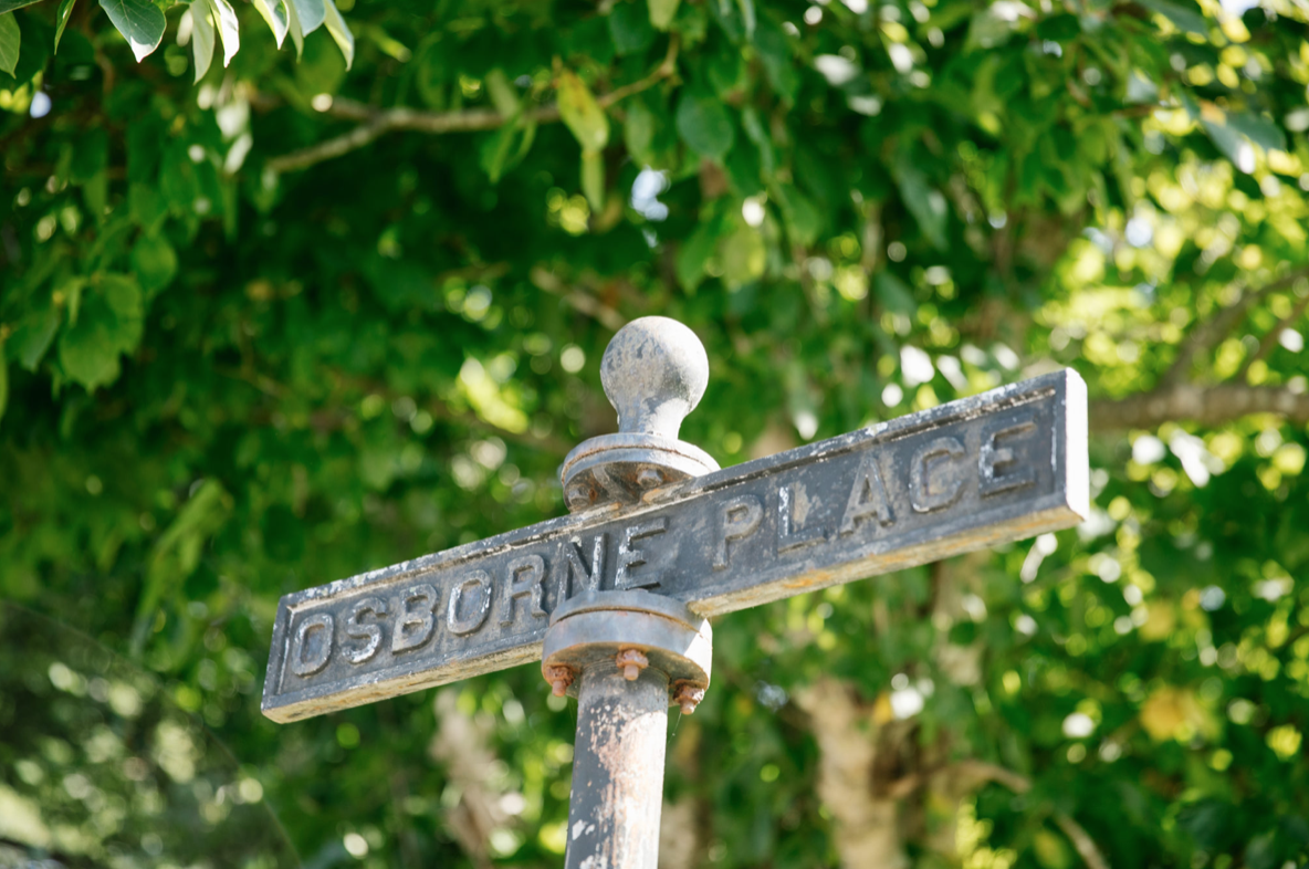 Close-up of an old street sign saying Osbourne Place against a background of green leaves.