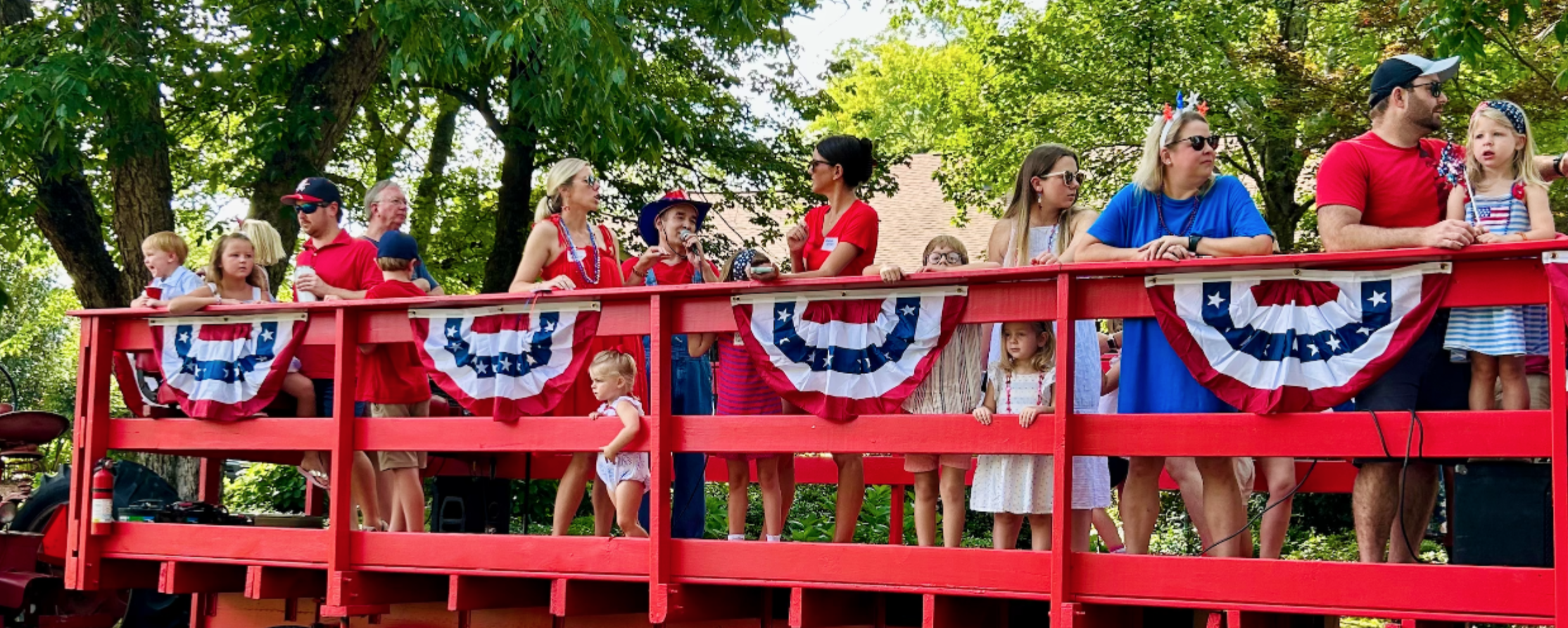 Celebrating Independence Day (4th of July) in Historic Ingleside with our neighbors, pulled by a tractor! A group of people standing on a decorated red tractor-pulled trailer during the parade, wearing red, white, and blue patriotic clothing.