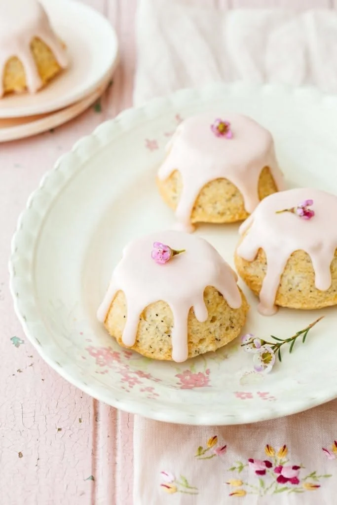 Three small coconut cakes with pink glaze and tiny pink flowers on top on a floral plate.