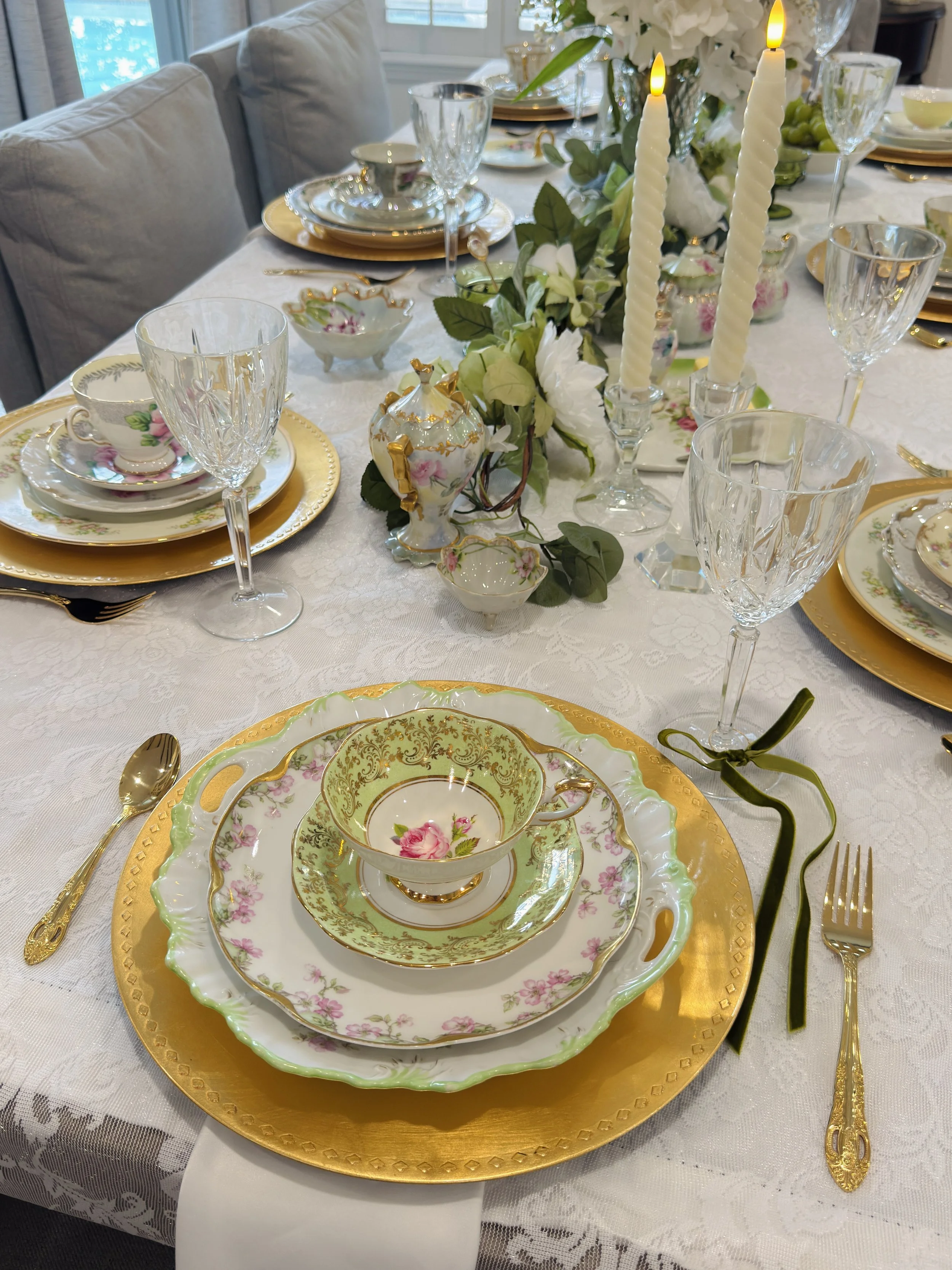 Elegant table setting with floral china, gold accents, crystal glassware, and a floral centerpiece with candles.