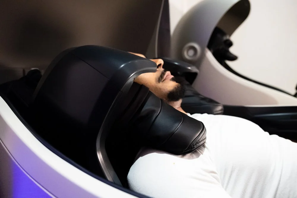 Person lying inside a futuristic massage machine, with their head resting on a cushioned support.