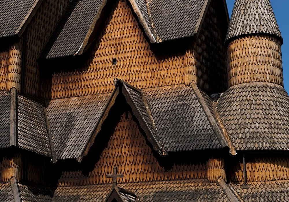 Close-up of a wooden church with overlapping fish scale shingles and several steeples with pointed roofs.
