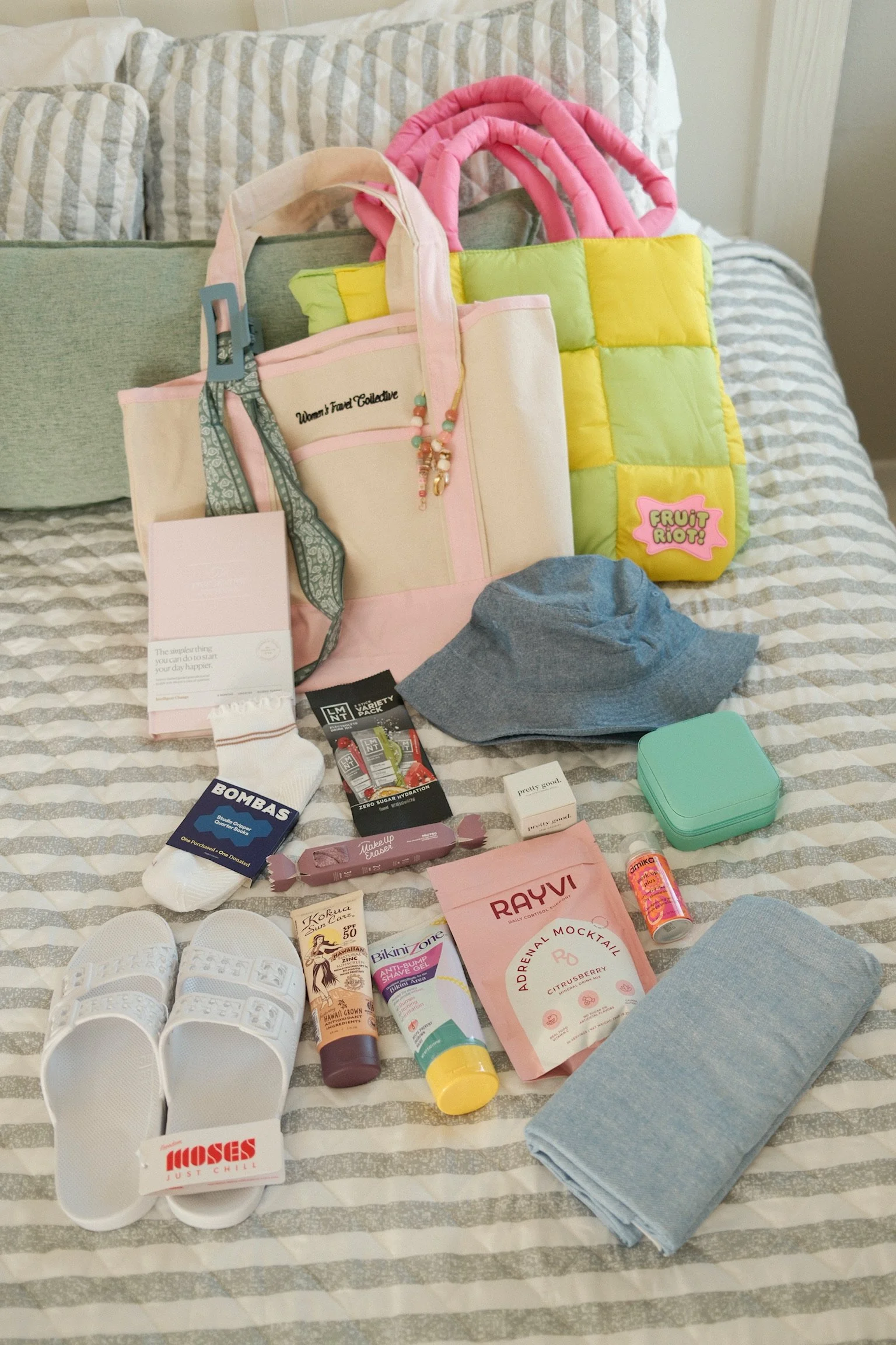Assorted personal care and fashion items spread on a bed, including shoes, socks, skincare products, a handbag, a small green container, a towel, a shirt, and various toiletries.