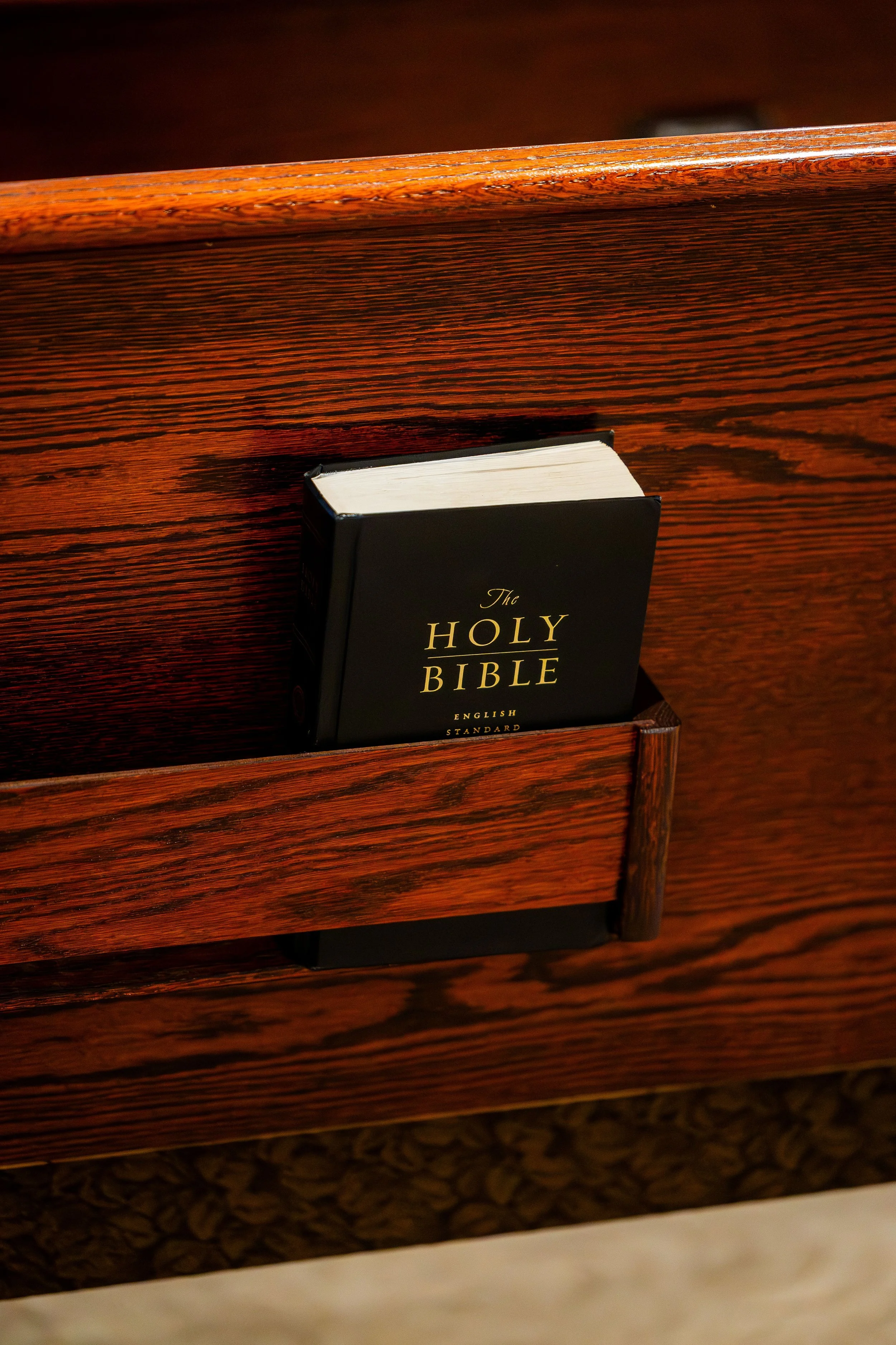 A Bible resting in a wooden pew, with a dark background.