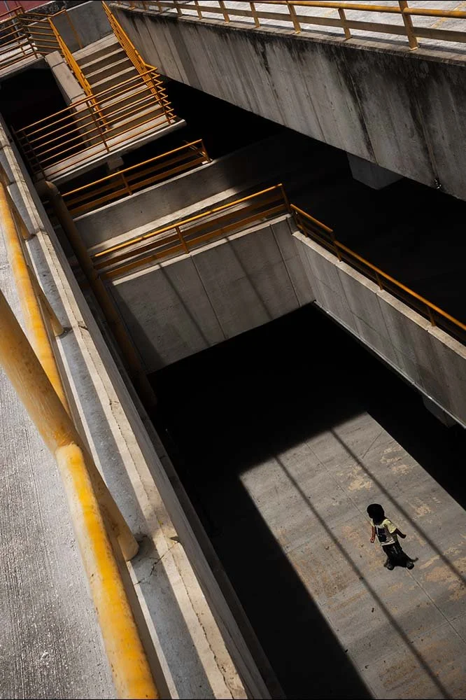 A person walking through an underground parking garage with concrete walls and yellow railings.