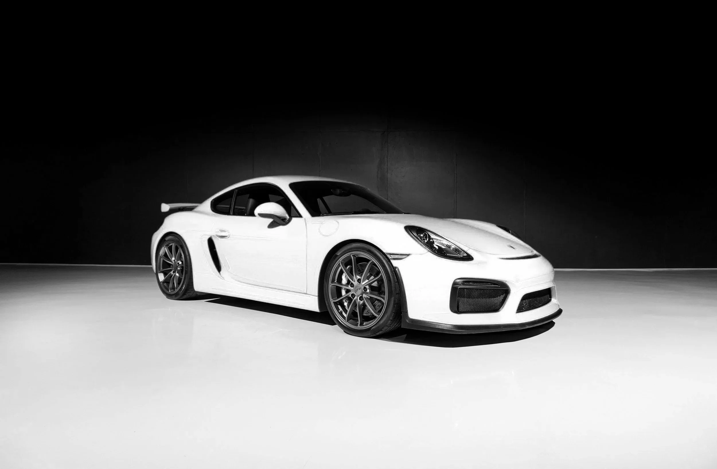A white sports car with black rims parked indoors against a dark background.