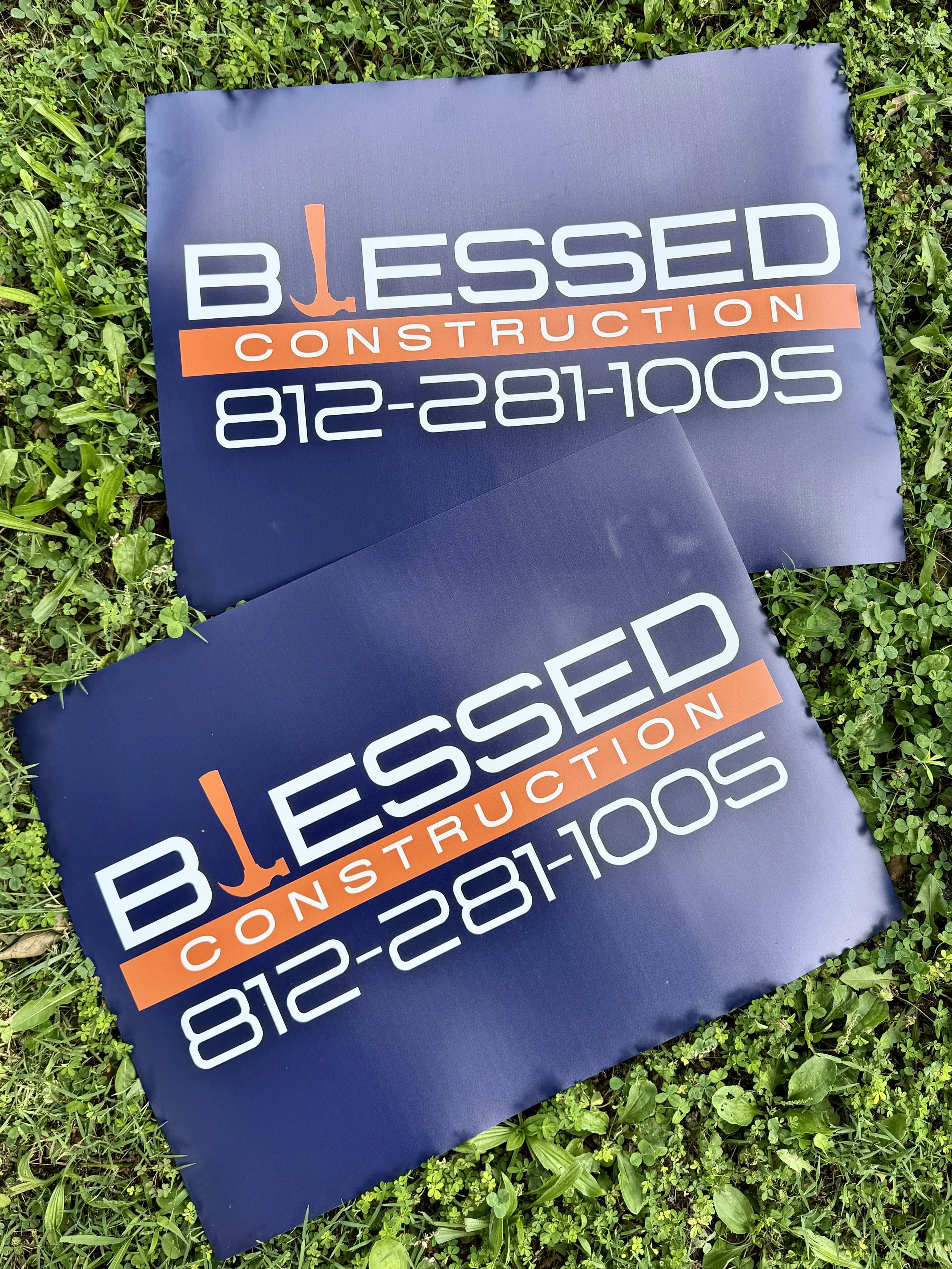 Sign for Blessed Construction with a phone number, placed on grass.