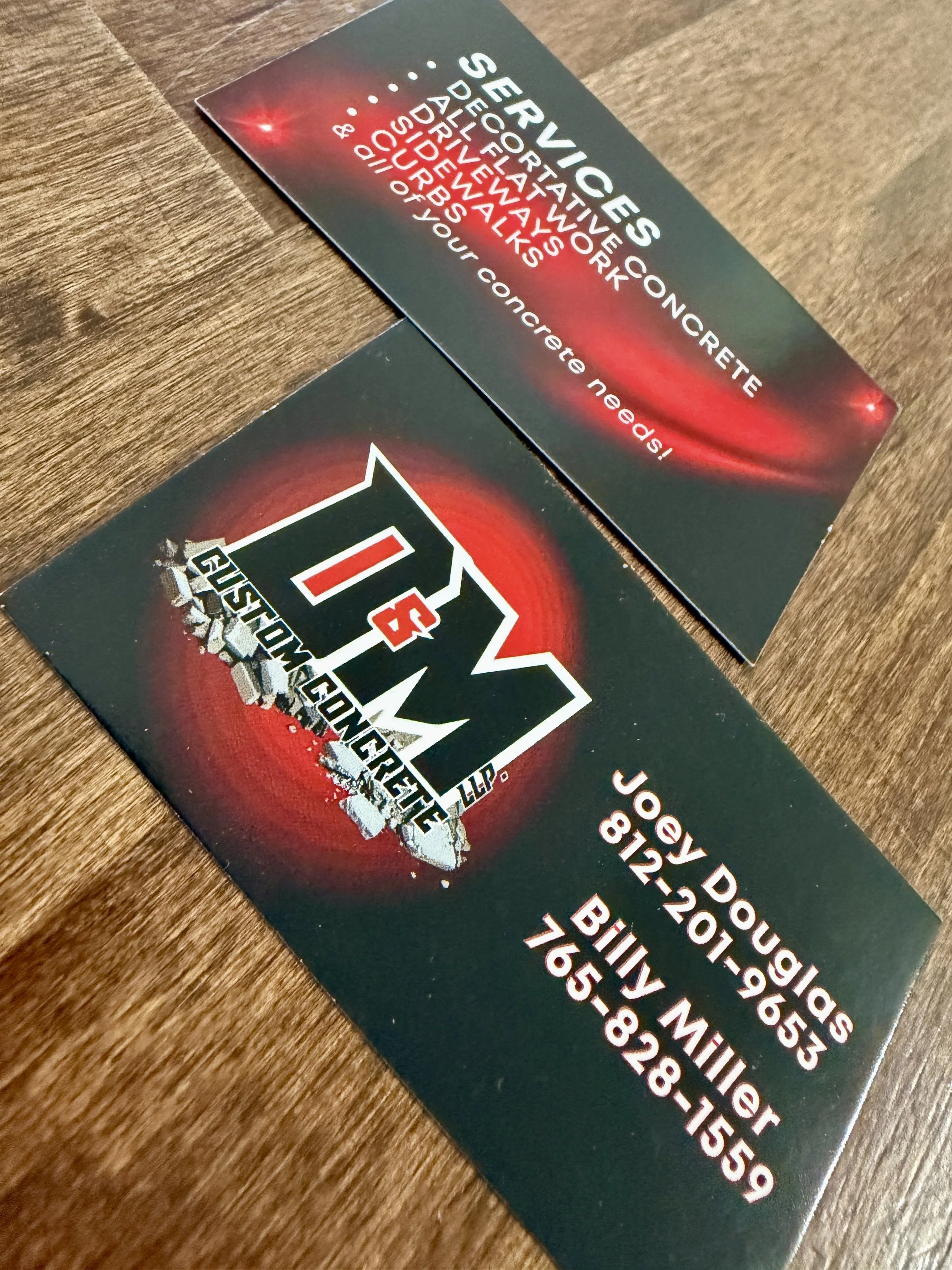 Close-up view of a business card with a black background featuring the logo and contact details, including name, phone number, and email, laid on a wooden surface.