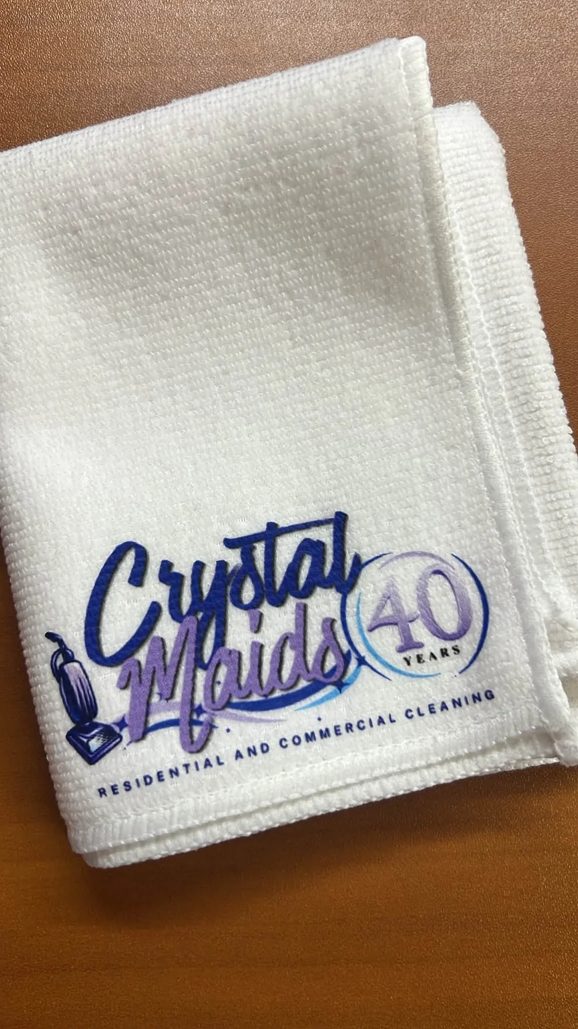A white cloth towel with blue and purple text and graphics, celebrating 40 years of residential and commercial cleaning, placed on a brown surface.