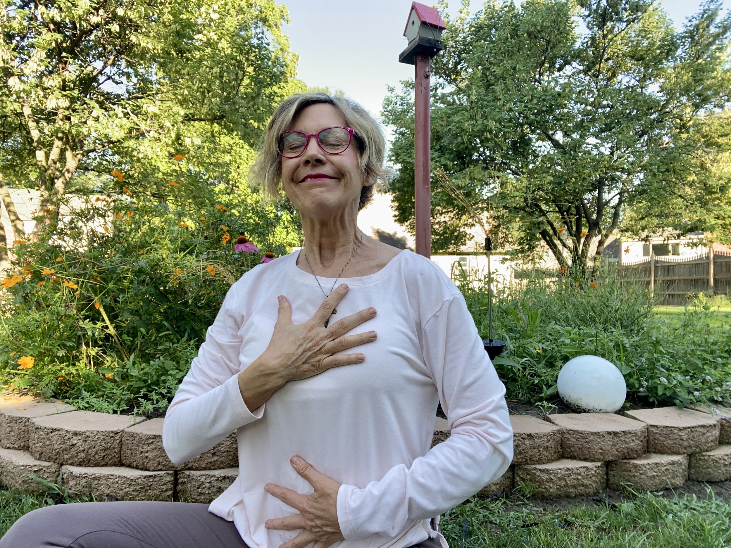 blonde woman with hand on heart sitting in garden eyes closed