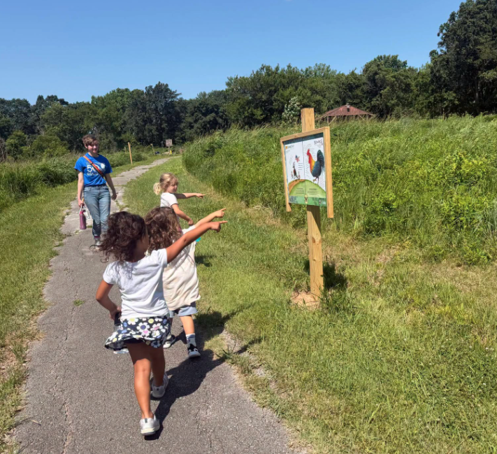 three children pointing at sign on trail