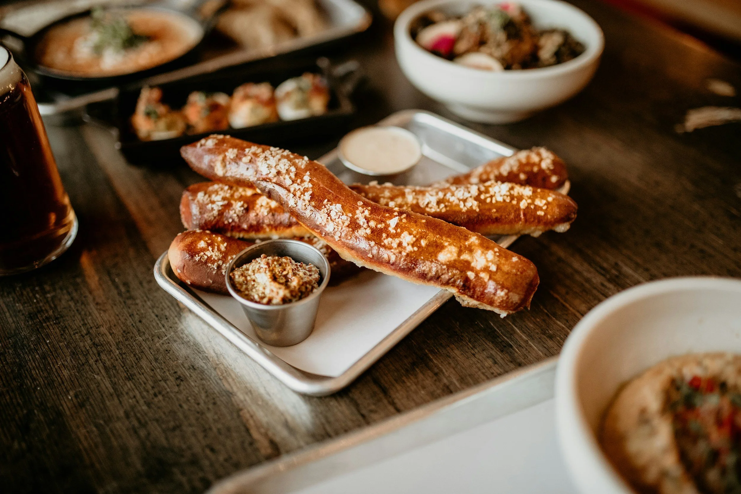 Close-up of a tray with breasdsticks and dipping sauces on a wooden table, with bowls of various dishes in the background.
