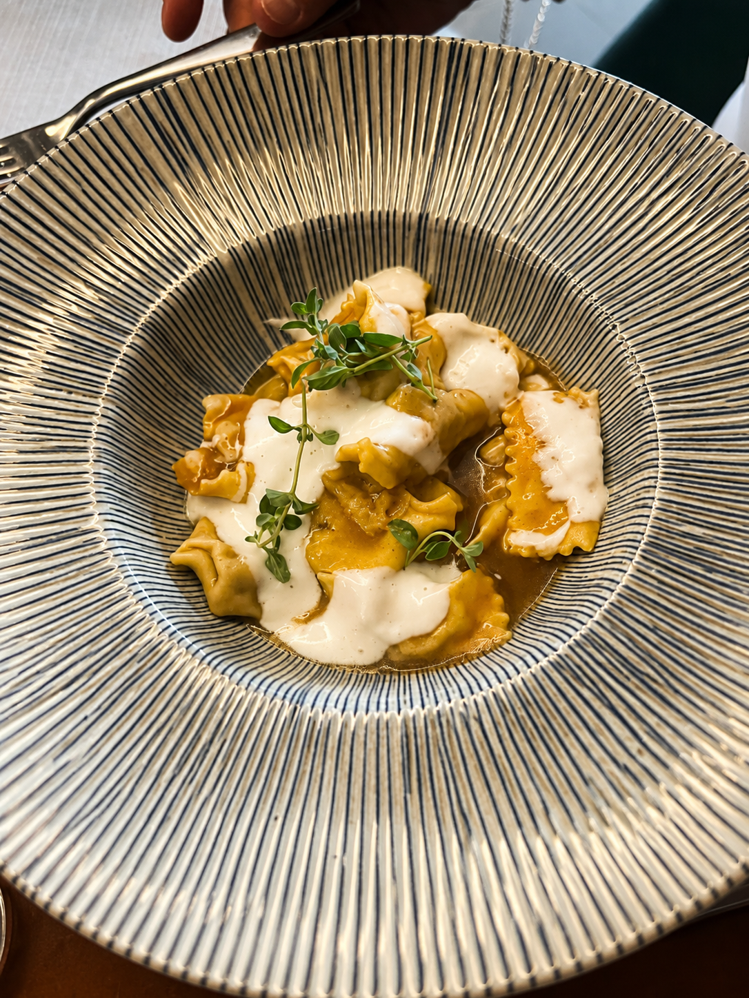 Piatto di pasta ripiena con salsa cremosa e decorato con erba aromatica in una ciotola con righe nere e beige.