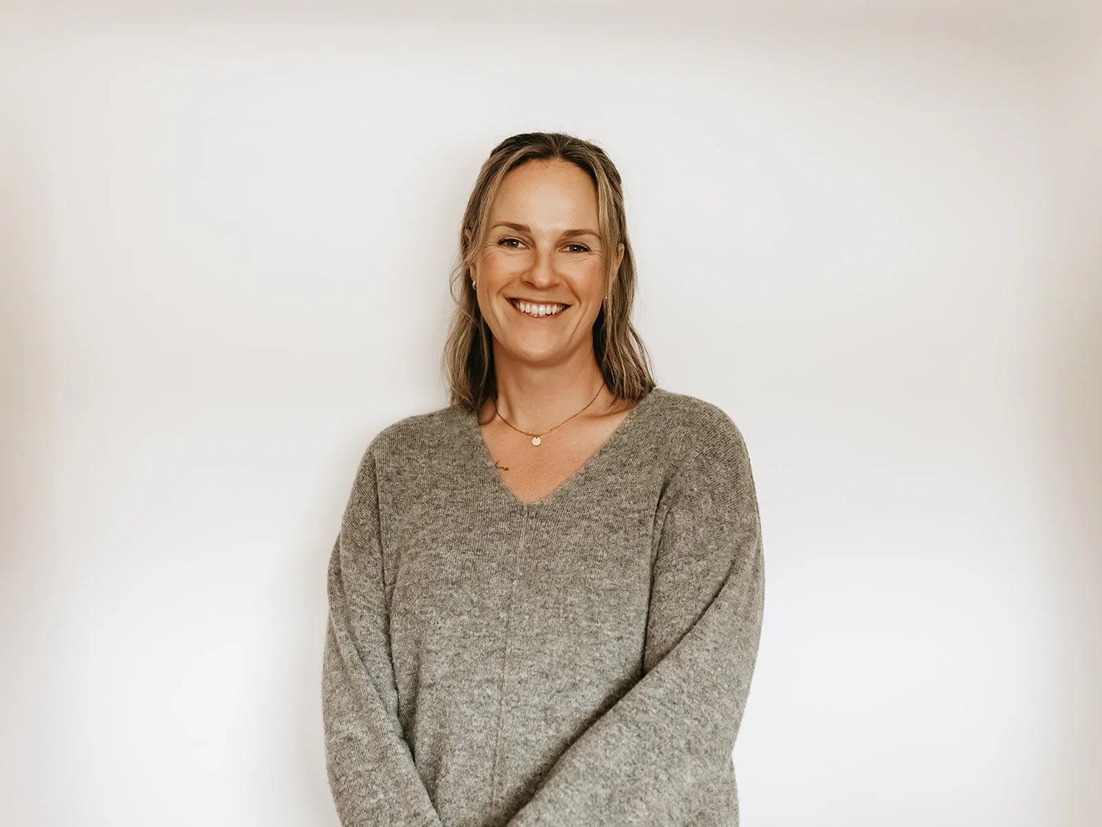 Woman with shoulder-length blonde hair and a gray sweater smiling against a plain white background.