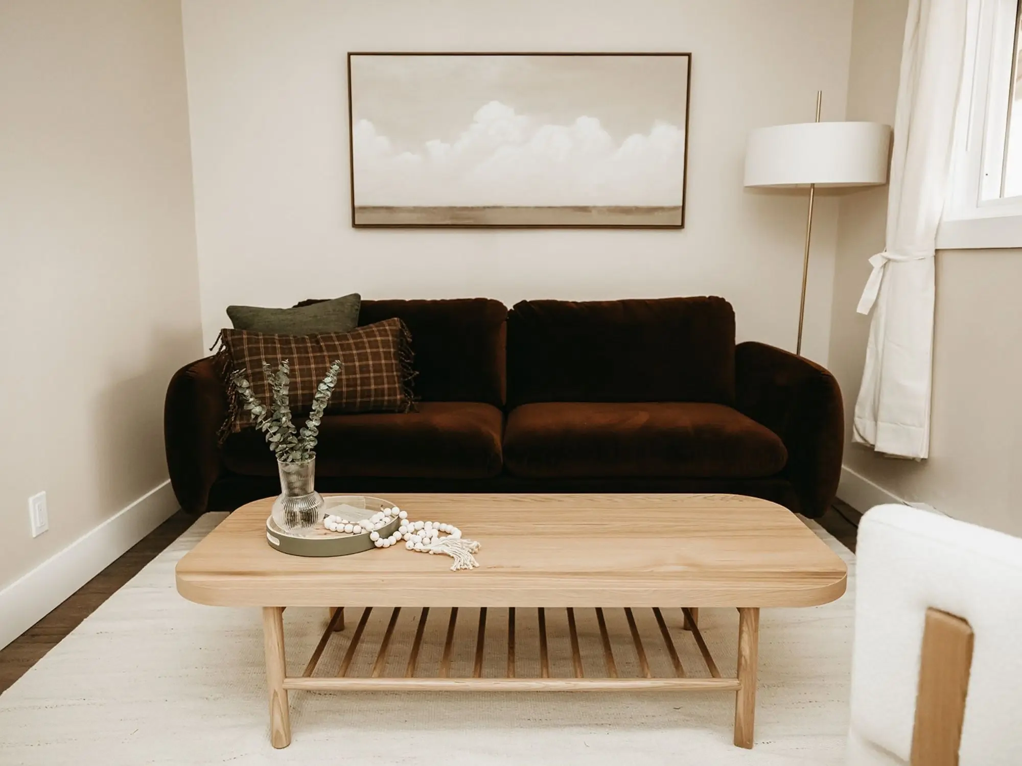 Living room with a brown sofa, a wooden coffee table, a tall floor lamp, and a window with white curtains.