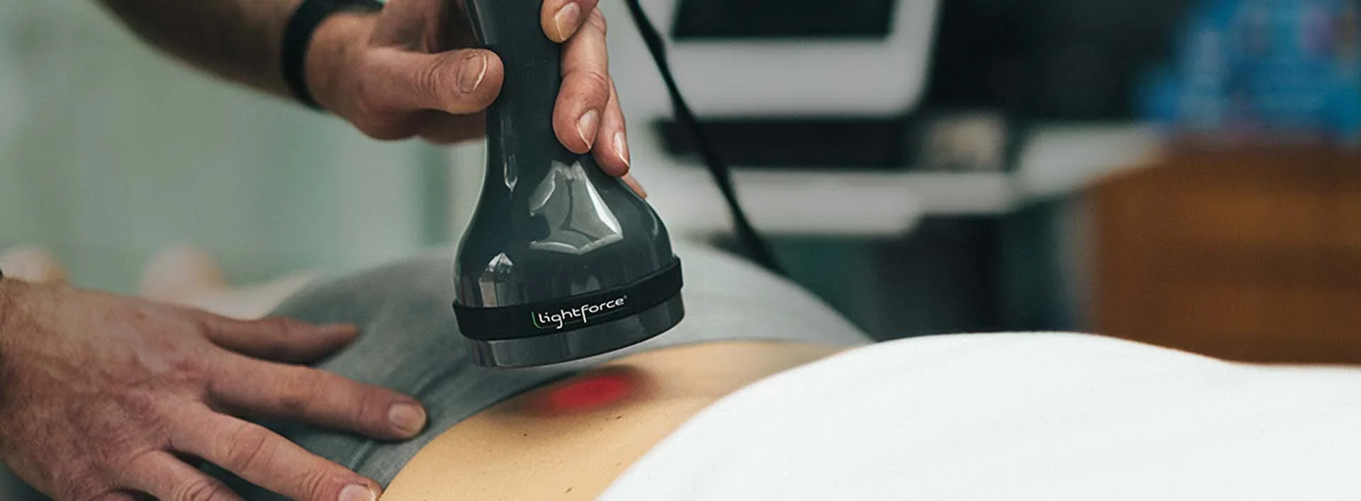 Medical professional using a Lightforce laser device on a patient's back for therapy or treatment.