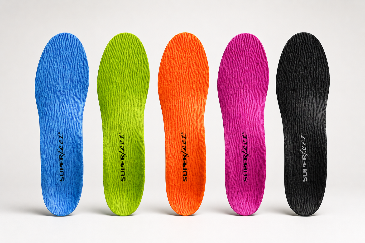 Five colorful superfeet orthotic insoles in blue, green, orange, pink, and black, arranged in a row on a white background.