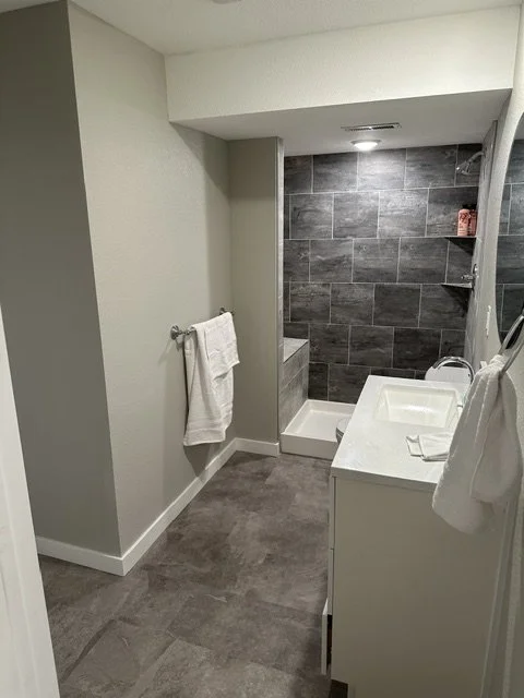 Small bathroom with a shower area, white vanity, and gray tiled wall in the shower.