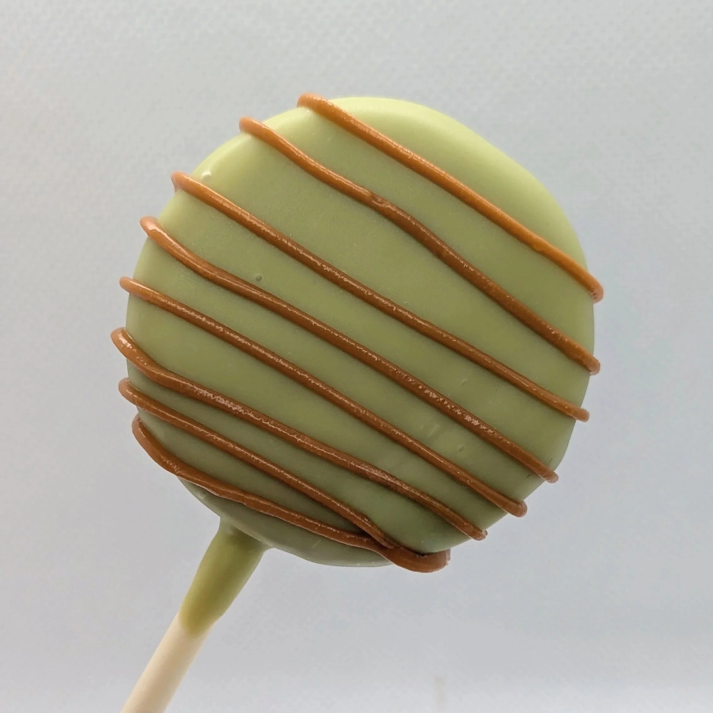 a single cake pop with apple green coating and lines of caramel colored chocolate drizzle.