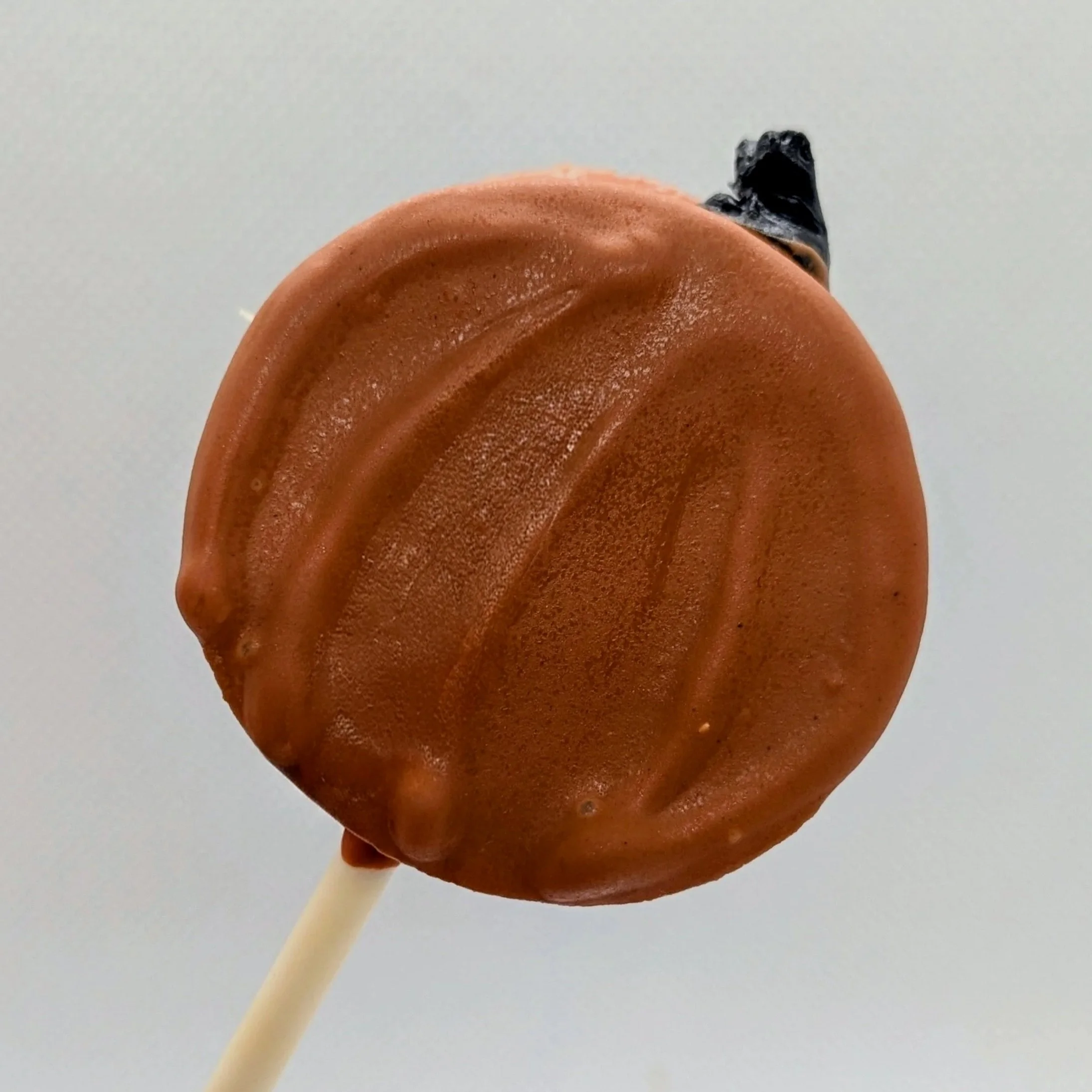 A single cake pop disc decorated to look like a pumpkin.